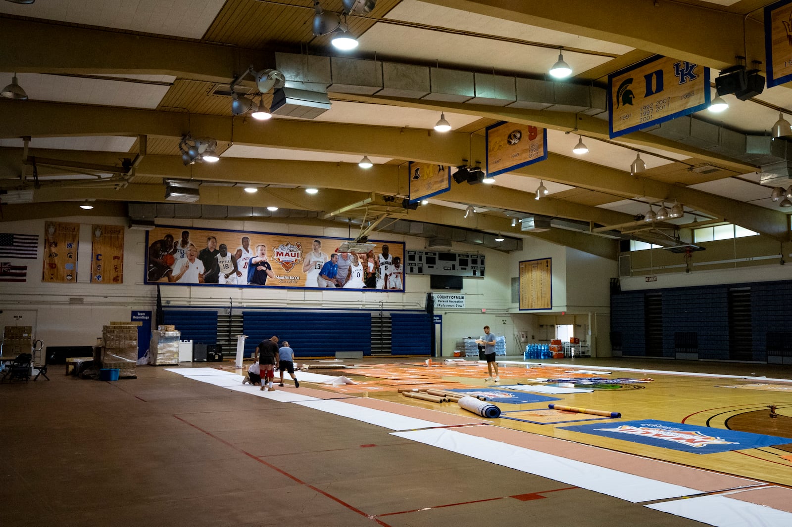 Workers set up banners and signs at Lahaina Civic Center, the venue for the Maui Invitational, Monday, Nov. 18, 2024, in Lahaina, Hawaii. The Maui Invitational is back in Lahaina, where eight of the NCAA's top men's basketball teams will compete in a three-day tournament. (AP Photo/Mengshin Lin)