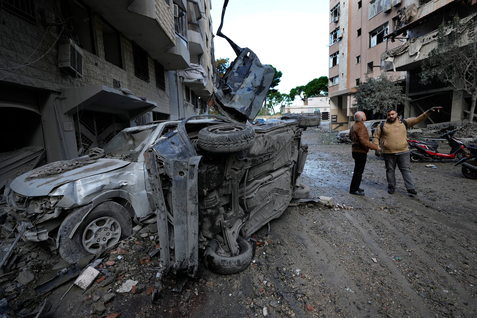 Residents stand near to cars that were destroyed after Sunday's Israeli airstrike in Dahiyeh, in the southern suburb of Beirut, Lebanon, Monday, Nov. 25, 2024. (AP Photo/Hussein Malla)