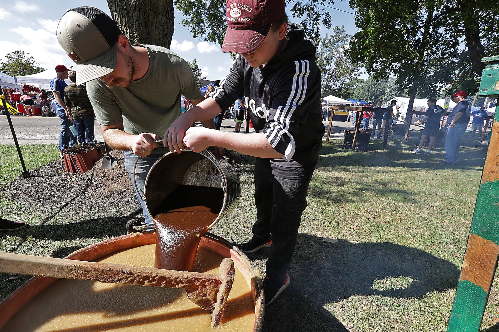 Jacob Juergens, left, and Caelek Stephany, both members of the Murphy family, pour the brown sugar mixture into one of the cauldrons of cooking apple butter at the Enon Apple Butter Festival. BILL LACKEY/STAFF 