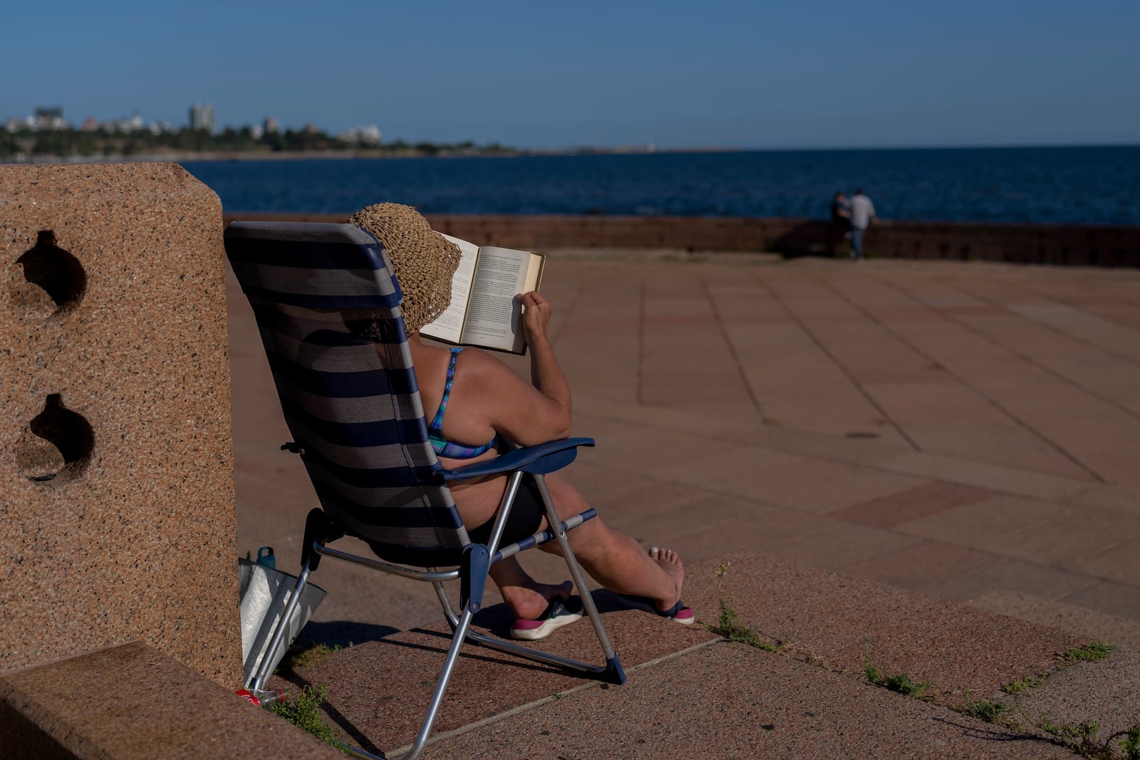 FILE - A woman reads a book while sunbathing during a summer day in Montevideo, Uruguay, Jan. 22, 2025. (AP Photo/Matilde Campodonico, File)