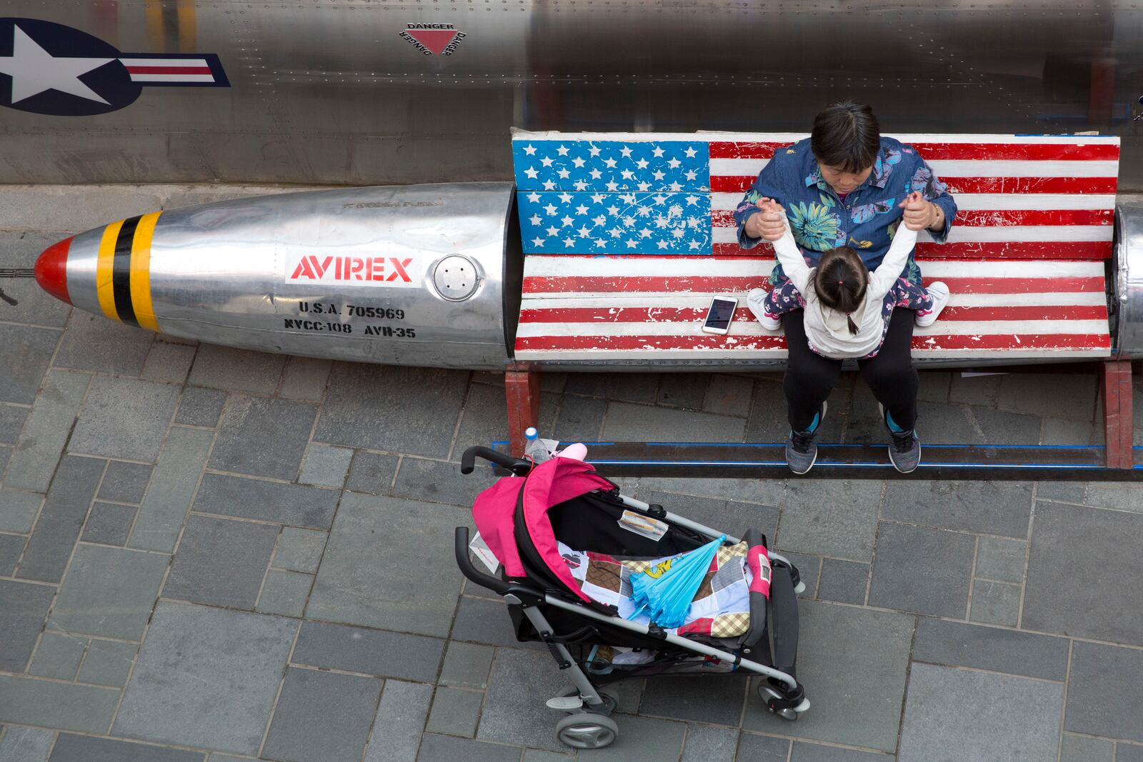 FILE - A woman tends to a child near a promotional gimmick in the form of a bomb and the U.S. flag outside a U.S. apparel shop in Beijing on April 12, 2018. (AP Photo/Ng Han Guan, File)