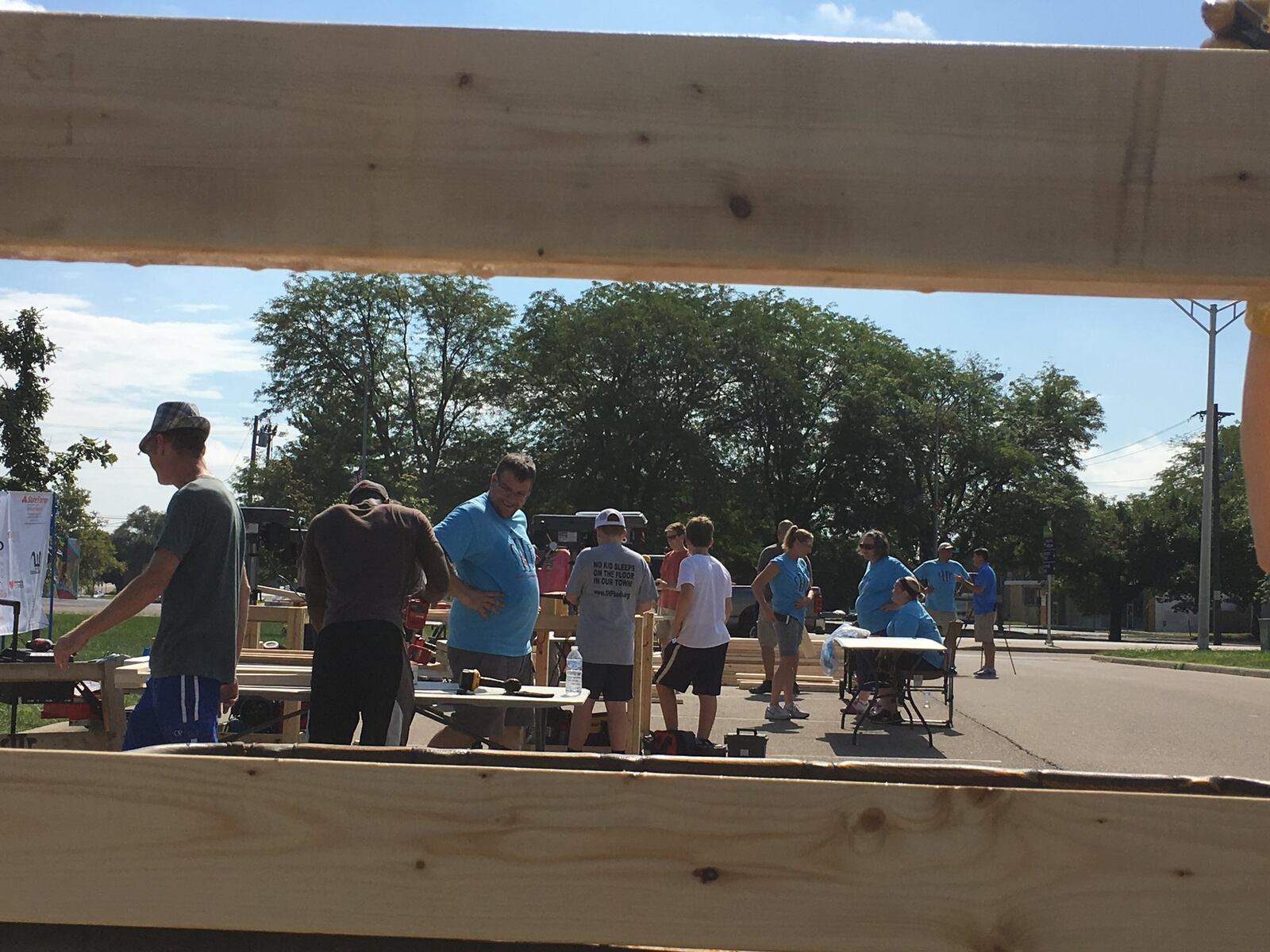 A section of a wooden bed, held by volunteers Laura Stanton, of Lebanon, and Julie Ring, of West Chester, frames others who spent Saturday building 30 beds for Sleep In Heavenly Peace.