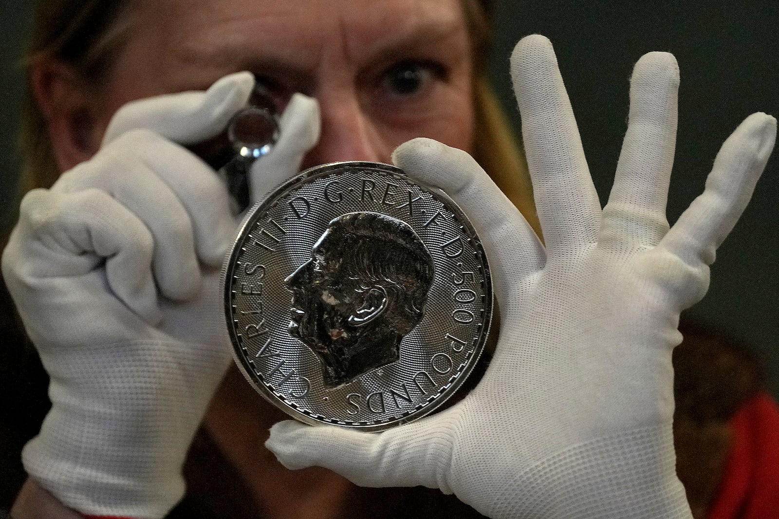 A warden looks through a magnifyer to check a 500 Pound coin during the "Trial of the Pyx,'' a ceremony that dates to the 12th Century in which coins are weighed in order to make certain they are up to standard, at the Goldsmiths' Hall in London, Tuesday, Feb. 11, 2025.(AP Photo/Frank Augstein)