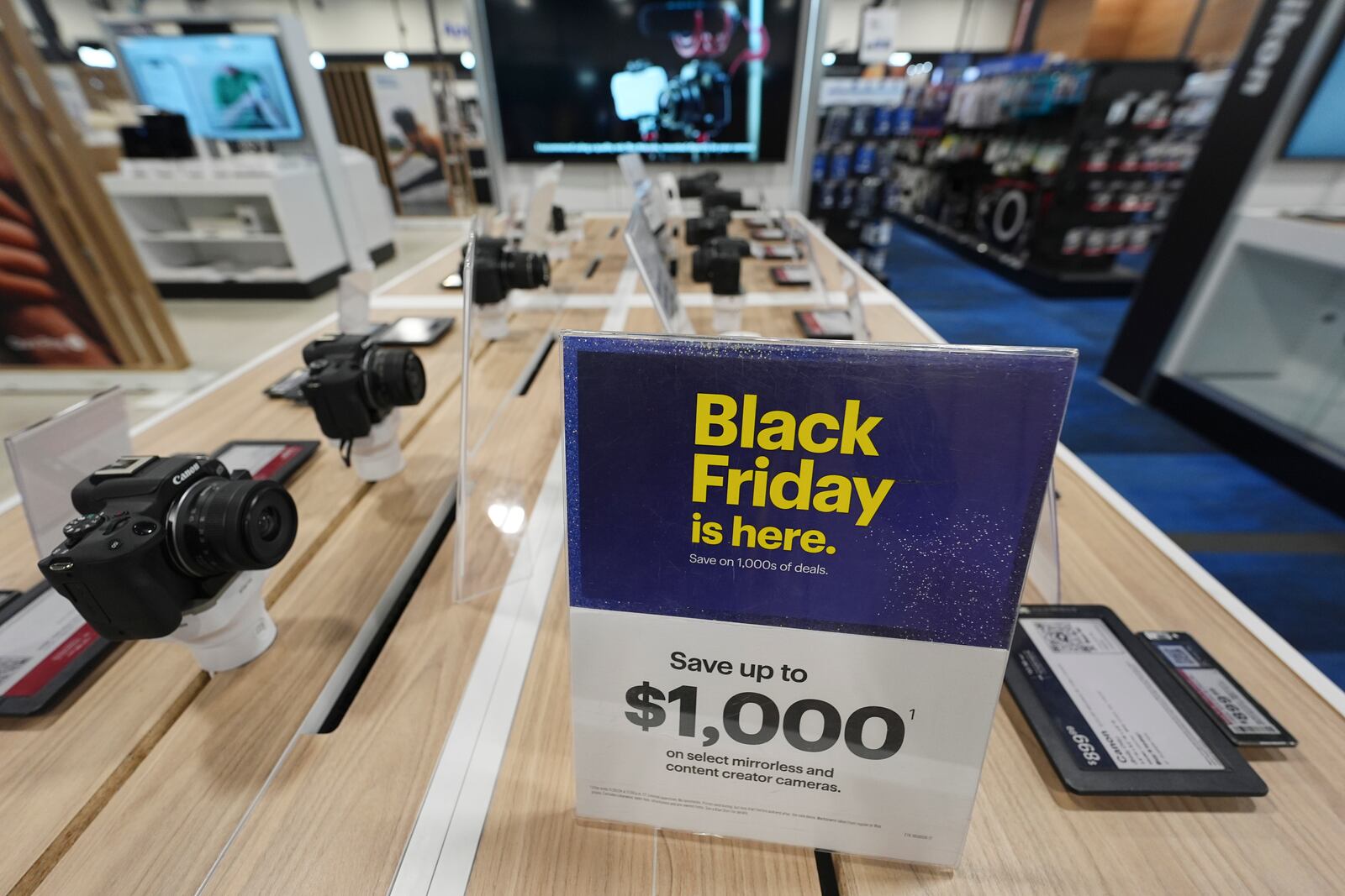 A sign promoting Black Friday deals sits on table with a display of mirrorless cameras in a Best Buy store Thursday, Nov. 21, 2024, in south Denver. (AP Photo/David Zalubowski)