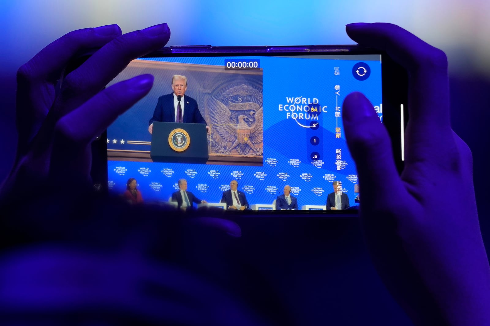 A woman takes pictures during a virtual speech of U.S. president Donald Trump at the Annual Meeting of World Economic Forum in Davos, Switzerland, Thursday, Jan. 23, 2025. (AP Photo/Markus Schreiber)