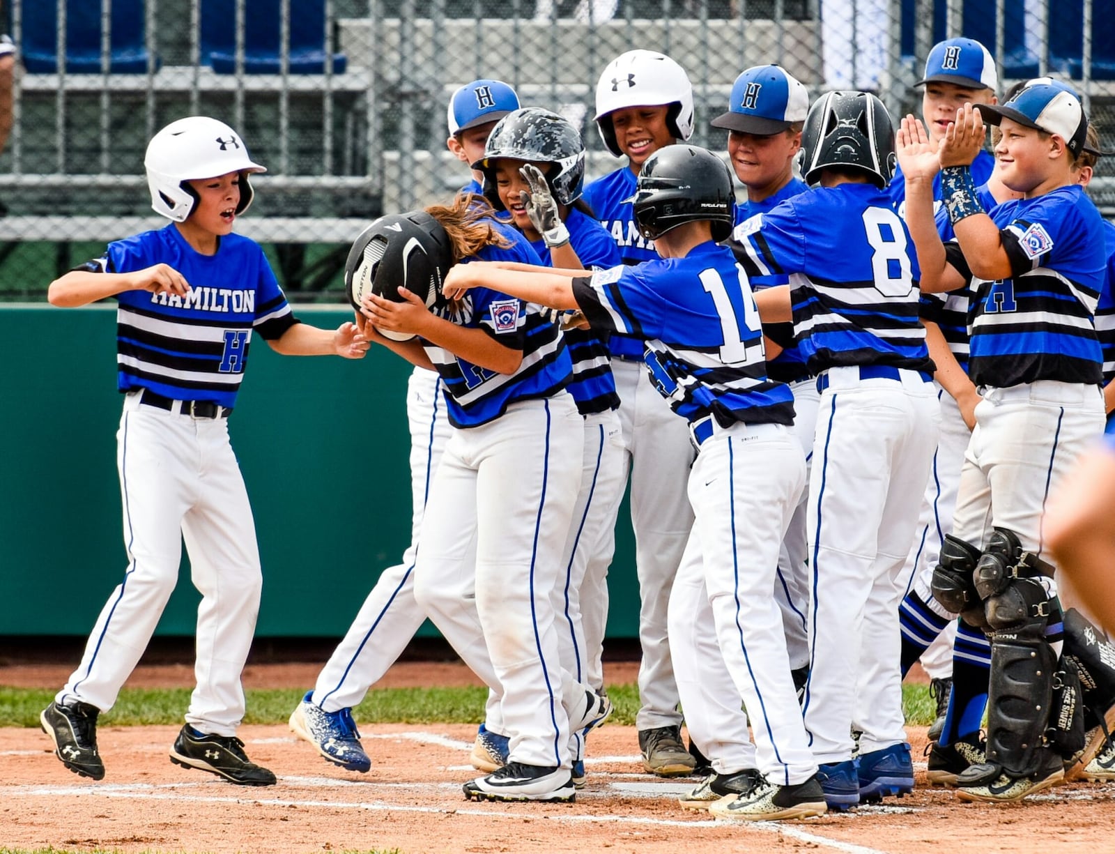 Hamilton West Side’s Jaycee Taylor is swarmed by her teammates after hitting a two-run homer Monday against Grosse Pointe Woods-Shores (Mich.) in the Little League Great Lakes Regional at Grand Park Sports Campus in Westfield, Ind. Hamilton won 10-2. NICK GRAHAM/STAFF