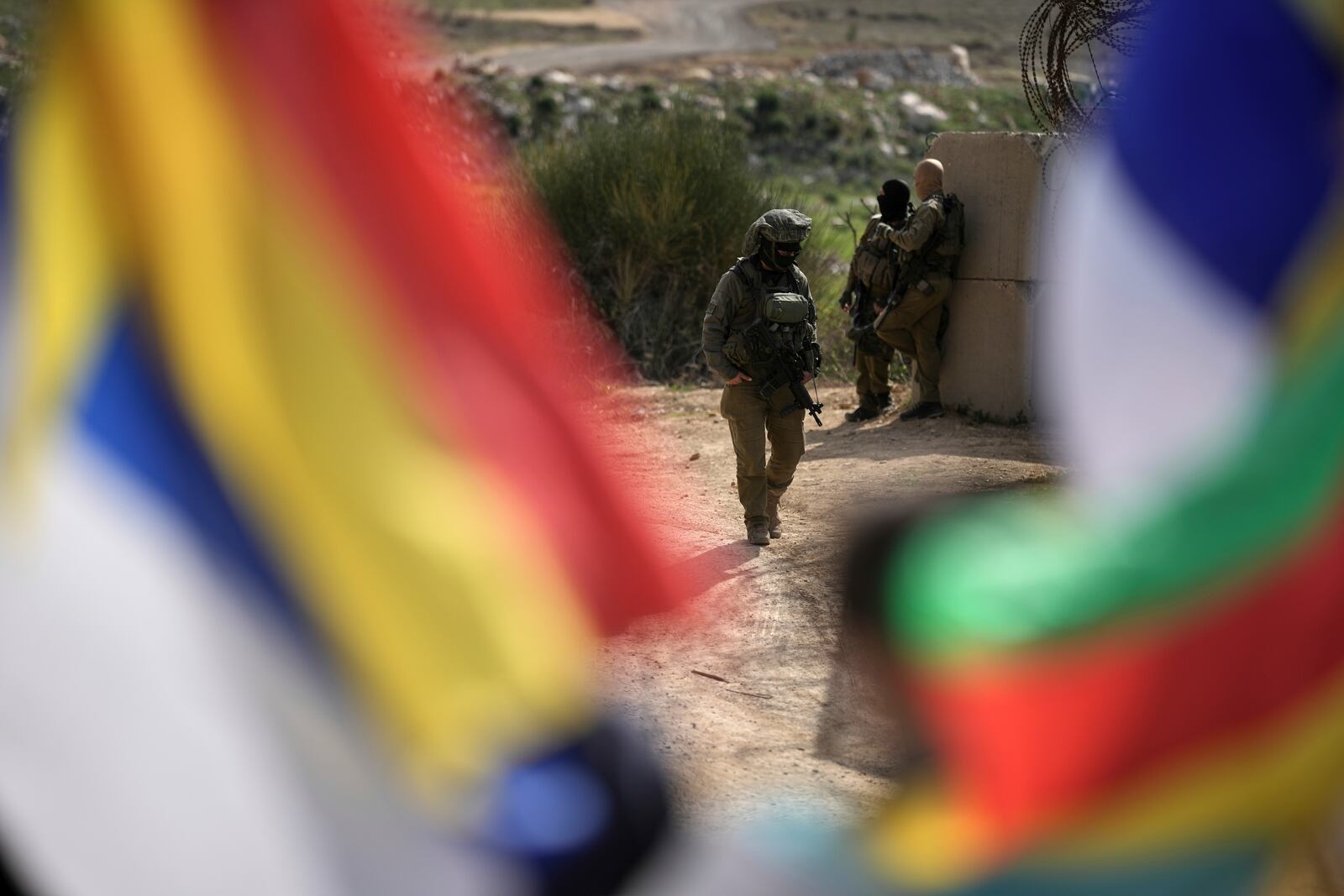 Israeli soldiers stand near members of the Druze community, holding Druze flags, as they wait for buses carrying members of the Syrian Druze community to cross from Syria into the village of Majdal Shams, located in the Israeli-controlled Golan Heights, on Friday, March 14, 2025. (AP Photo/Leo Correa)