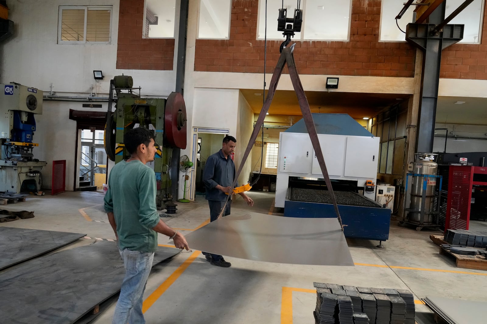 Workers move a large steel sheet to place in a laser cutting machine at a factory in a suburb of Bengaluru, India, Thursday, Feb. 27, 2025. (AP Photo/Aijaz Rahi)