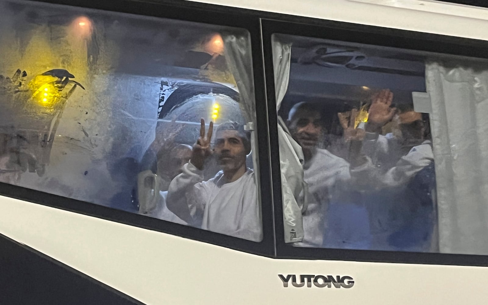 Palestinian prisoners deported outside the Palestinian Territories, wave after being released from Israeli prison, following a ceasefire agreement between Israel and Hamas, as they arrive at the Egyptian side of the Rafah border crossing between Egypt and the Gaza Strip, Thursday, Feb. 27, 2025. (AP Photo/Mohamed Arafat)