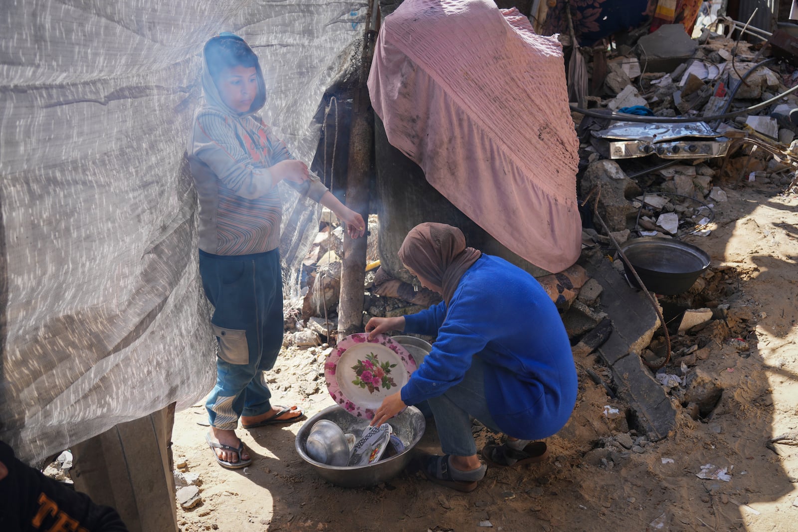 Rawya Tamboura and her son Yazan wash dishes next to their home, which was struck by an Israeli airstrike on Oct. 20, 2023, in Beit Lahiya, northern Gaza Strip, Friday, Feb. 21, 2025. (AP Photo/Abdel Kareem Hana)