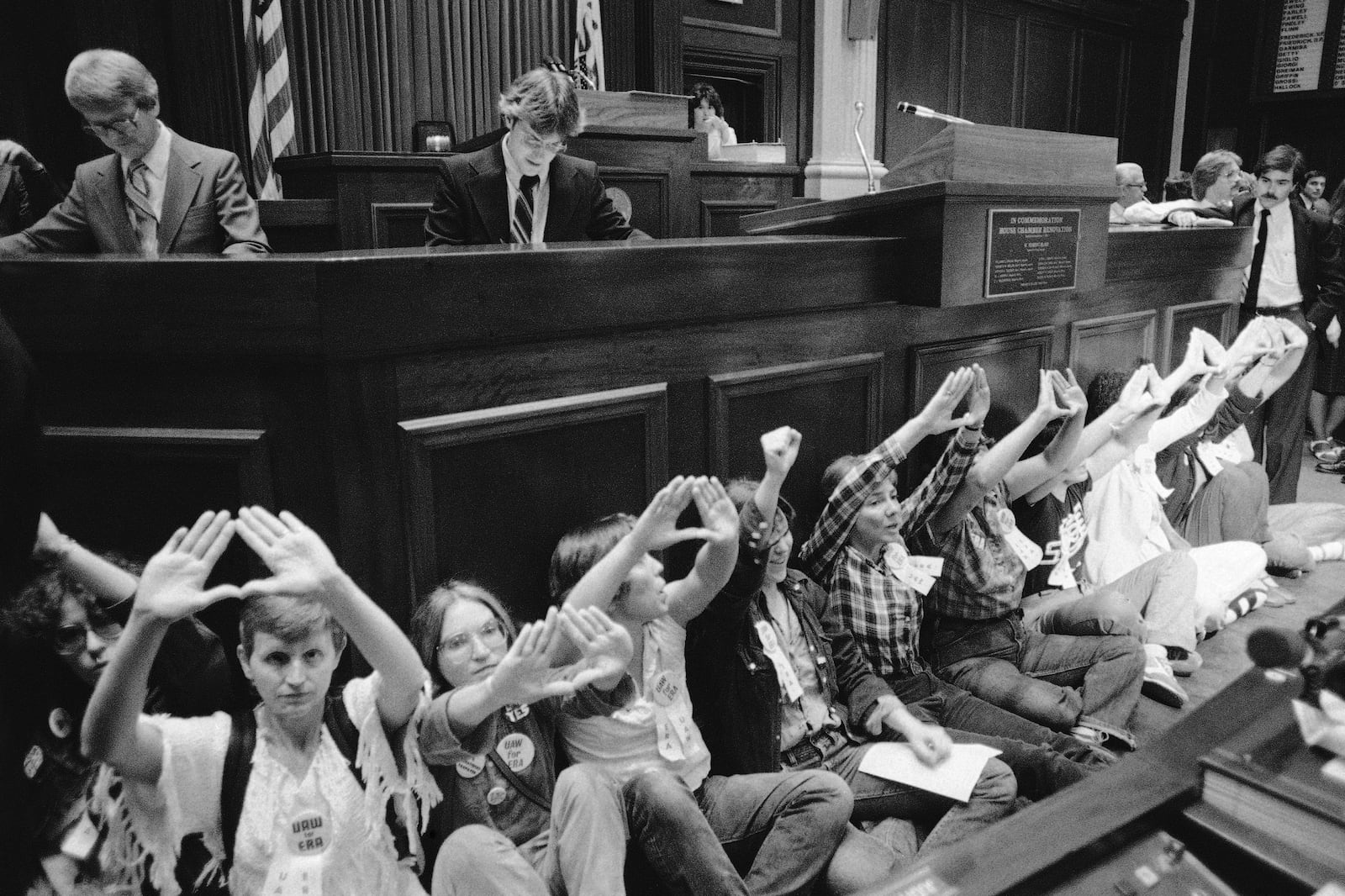 FILE - A group of women, who had earlier chained themselves to the door of the Senate and blocked the door to the Governor's office, give the sign for a female, as they disrupt the Illinois House in Springfield, Ill., on Wednesday, June 17, 1982. (AP Photo/Charles Bennett, File)