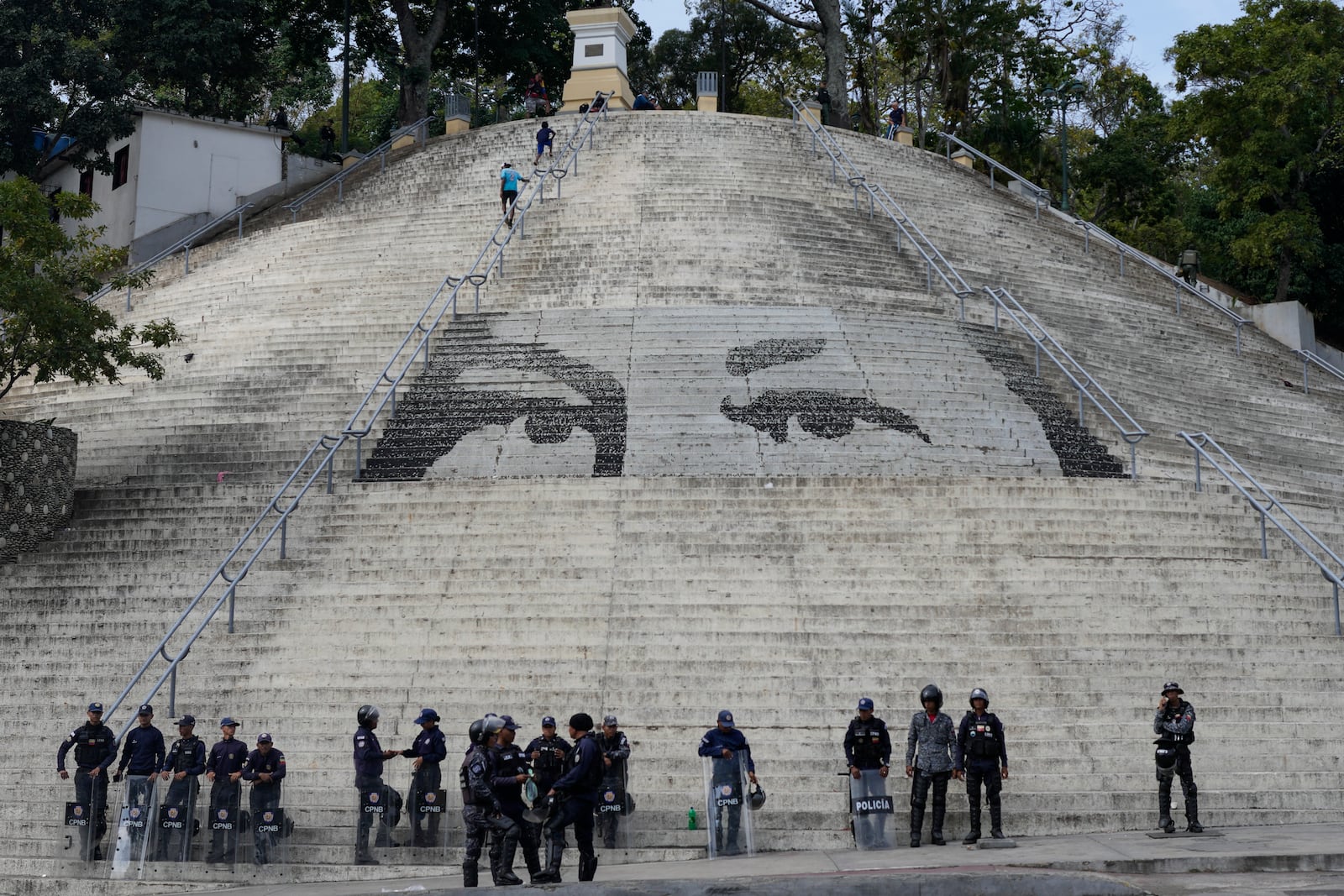 Bolivarian National Police stand guard in front of steps featuring a giant portrait of the eyes of the late President Hugo Chavez ahead of President Nicolas Maduro's swearing-in for a third term, in Caracas, Venezuela, Sunday, Jan. 5, 2025. (AP Photo/Matias Delacroix)