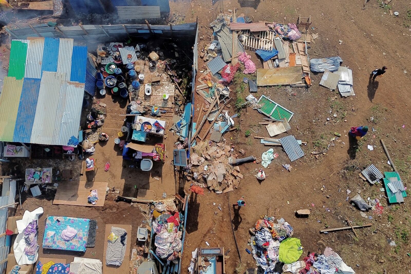 People walk by destroyed homes in the Barakani, Mayotte, informal settlement, Saturday, Dec. 21, 2024. (AP Photo/Adrienne Surprenant)