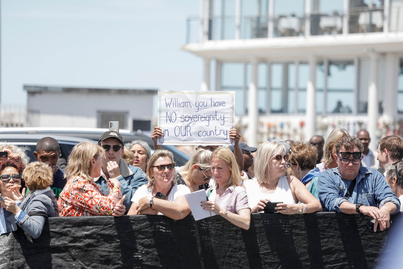 A person holds a placard that reads "William, you have no sovereignty in our country" while a crowd gathers to see Britain's Prince William (unseen) meeting local fisherman in Kalk Bay Harbour, near Cape Town, South Africa Thursday, Nov. 7, 2024. (Gianluigi Guercia/Pool Photo via AP)