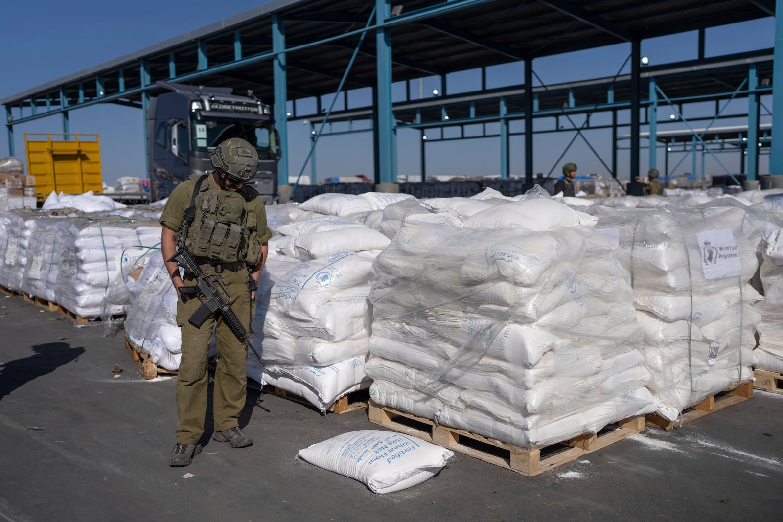 An Israeli soldier stands guard on the Palestinian side of the Kerem Shalom aid crossing as reporters tour the area where aid awaits pickup in the Gaza Strip, Thursday, Dec. 19, 2024. (AP Photo/Ohad Zwigenberg)