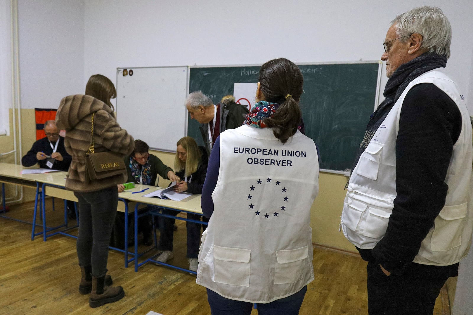 European Union election observers watch a voter at a polling station during a parliamentary election in the northern Serb-dominated part of ethnically divided town of Mitrovica, Kosovo, Sunday, Feb. 9, 2025. (AP Photo/Bojan Slavkovic)