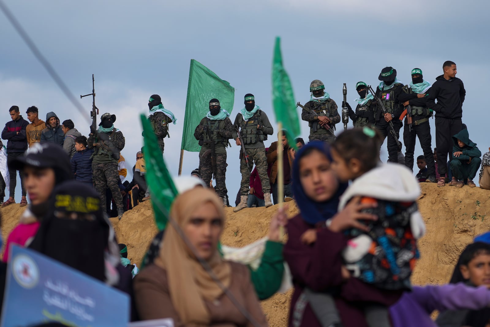 Palestinians watch as Hamas fighters take up a position ahead of handing over the bodies of four Israeli hostages, including a mother and her two children, who had long been feared dead, to the Red Cross in Khan Younis, southern Gaza Strip, Thursday, Feb. 20, 2025. (AP Photo/Abdel Kareem Hana)