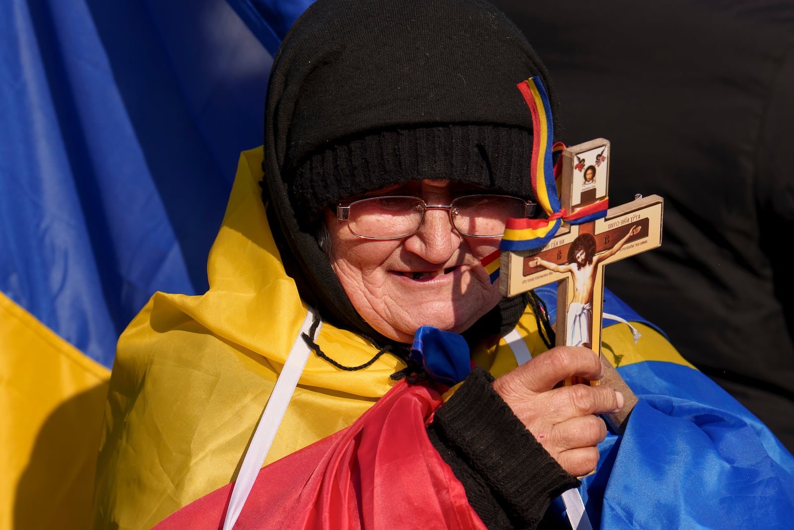 A woman drapped in the Romanian flag holds a cross during a protest by supporters of Calin Georgescu, the winner of Romania's first round of presidential election which the Constitutional Court later annulled in Bucharest, Romania, Monday, Feb. 10, 2025. (AP Photo/Vadim Ghirda)