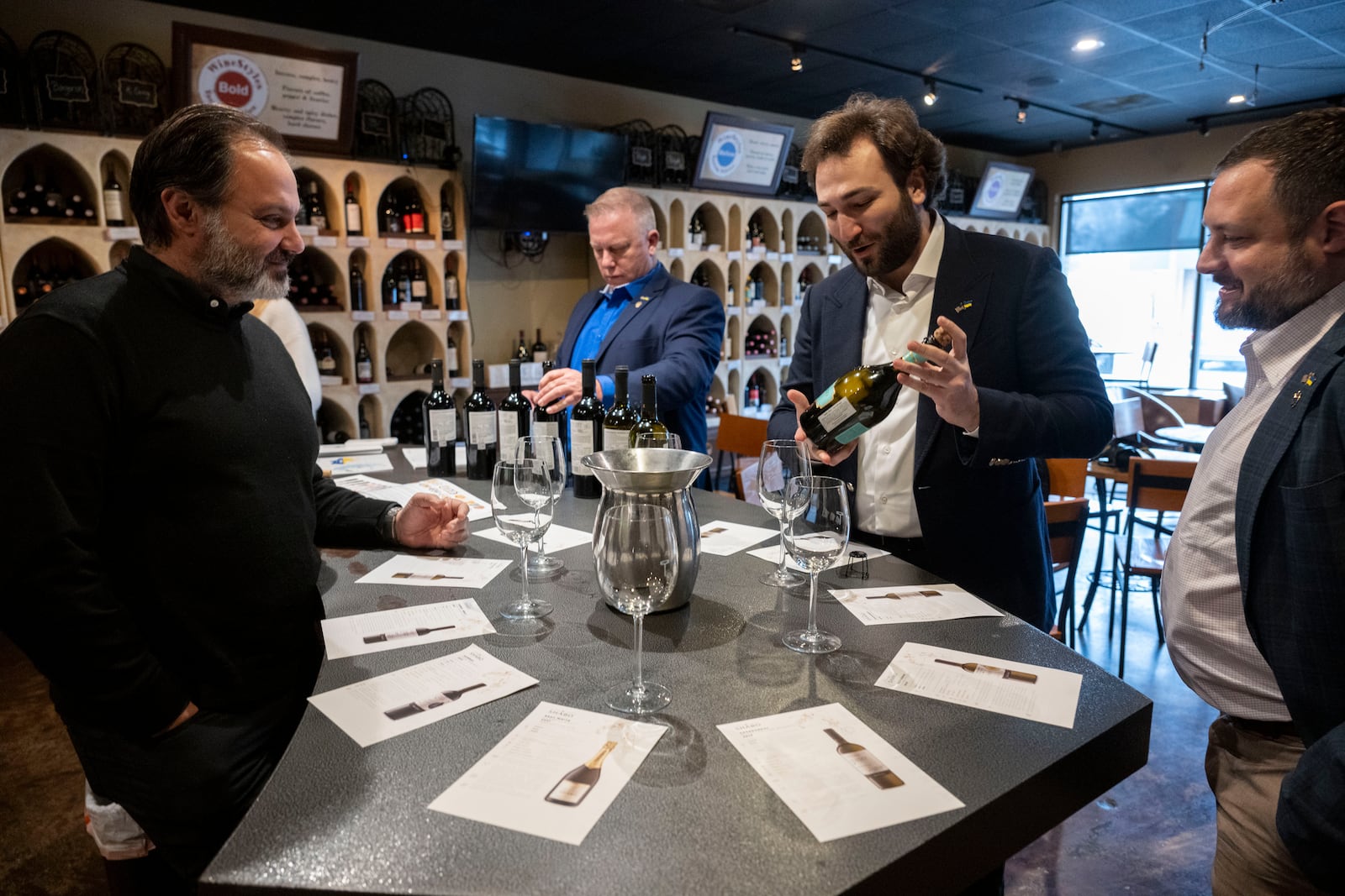 Giorgi Iukuridze, owner and CEO Shabo, a Ukrainian winery, second from right, show one of his wines to the owner of Wine Styles Arthur Lampros, left, at the start of a wine tasting at Wine Styles, Dec. 20, 2024 in Dumfries, Va. At the tasting table with Iukuridze are Sam Lerman, CEO of SPYRT Worldwide, right, and Joseph Belli, Sales Manager for SPYRT Worldwide. (AP Photo/Kevin Wolf)