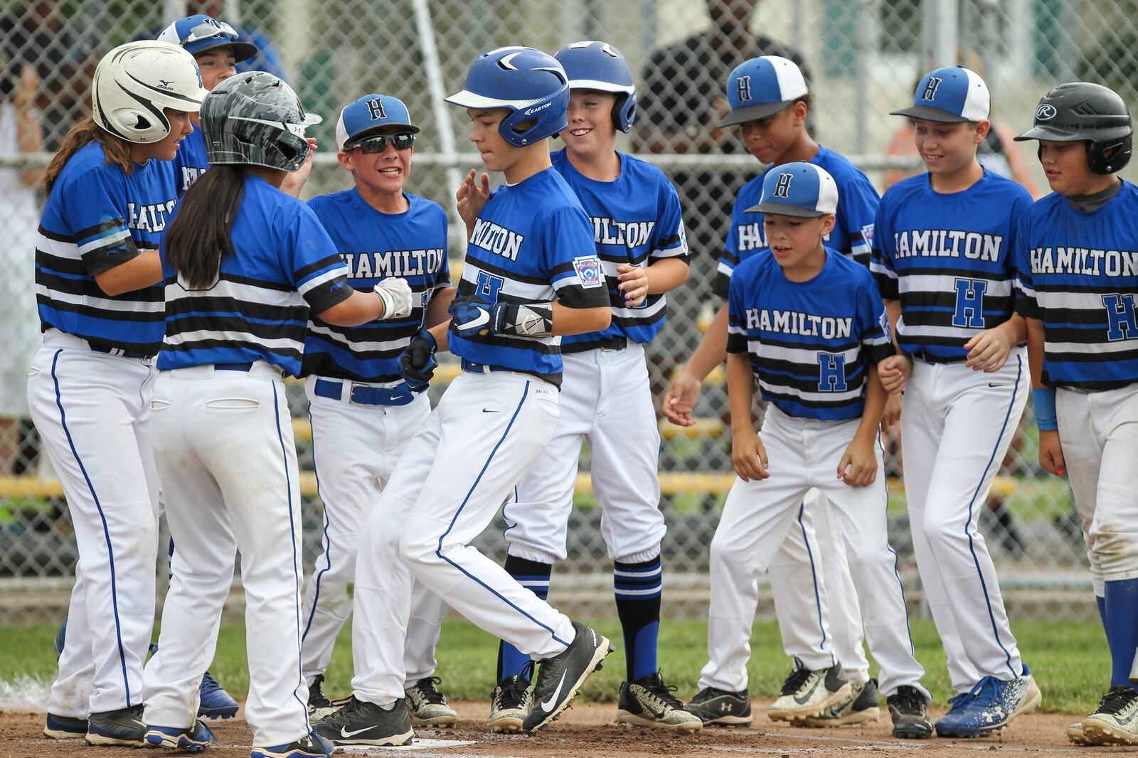 Hamilton West Side’s Lake Cundiff is greeted by his teammates at home plate after hitting a first-inning home run Thursday against Canfield in the winners’ bracket final of the Ohio Little League 12-year-old baseball tournament at Ford Park in Maumee. CONTRIBUTED PHOTO BY SCOTT GRAU