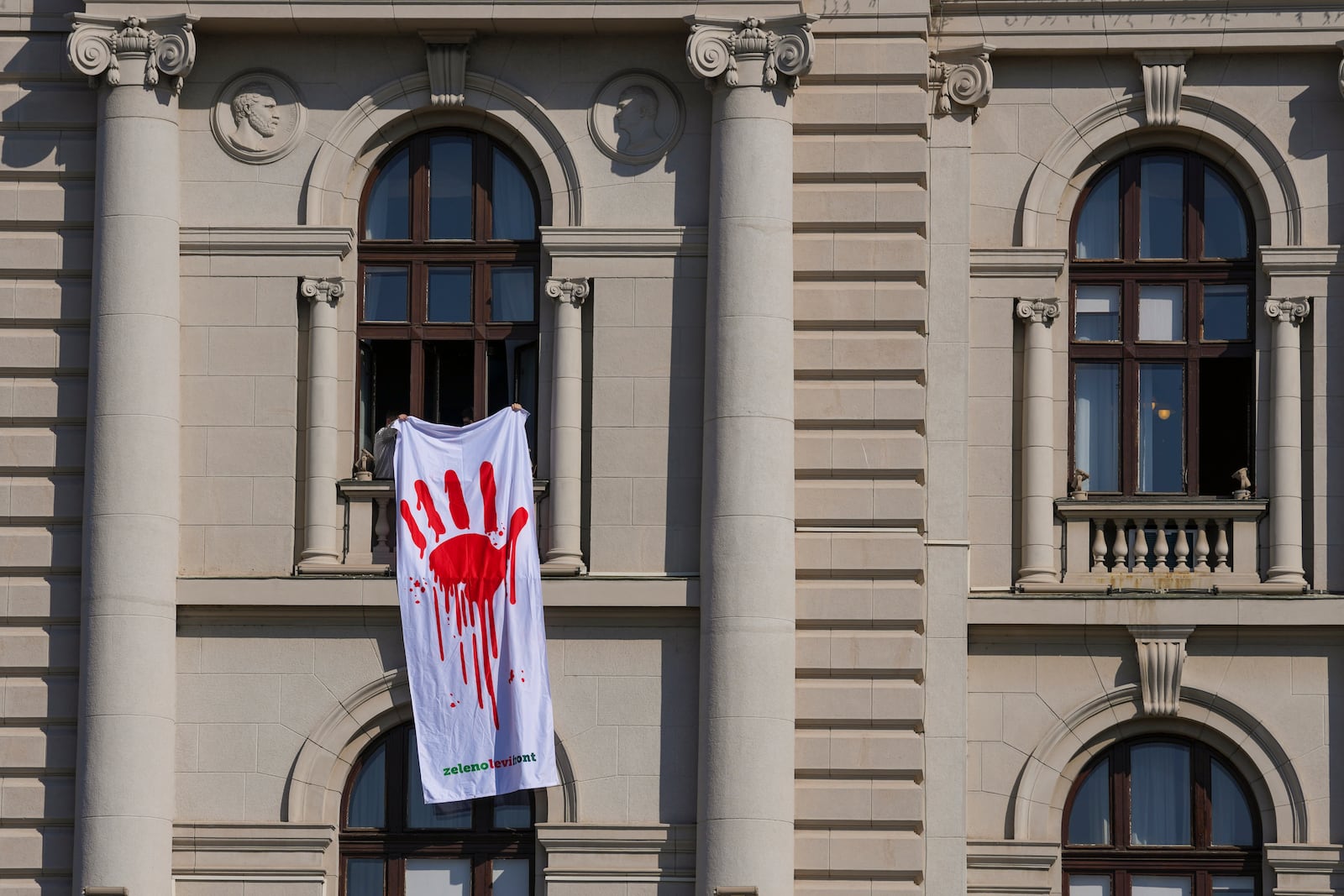 Opposition lawmakers hold a banner that shows a painted hand symbolizing blood, during a parliament session in Belgrade, Serbia, Tuesday, March 4, 2025. (AP Photo/Darko Vojinovic)