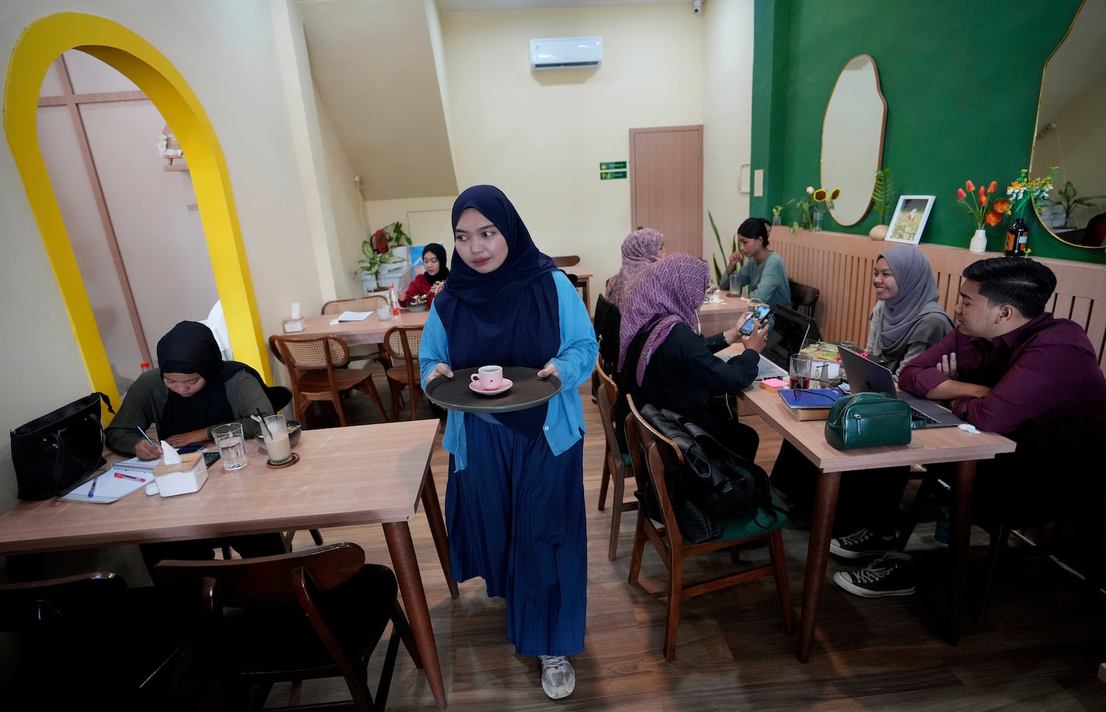 Qurrata Ayuni, a 28-year-old tsunami survivor, serves customers at the cafe she runs in Banda Aceh, Indonesia, Wednesday, Dec. 11, 2024. (AP Photo/Achmad Ibrahim)