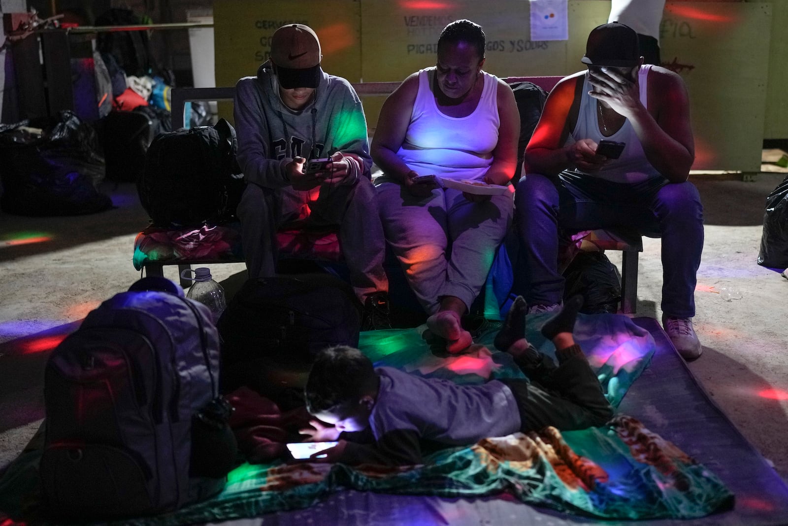 Venezuelan migrants check their phones as they spend the night in Puerto Cartí, on Panama's Caribbean coast, Sunday, Feb. 23, 2025, from which they plan to take a boat to Colombia after giving up hopes of reaching the U.S. amid President Trump's crackdown on migration. (AP Photo/Matias Delacroix)