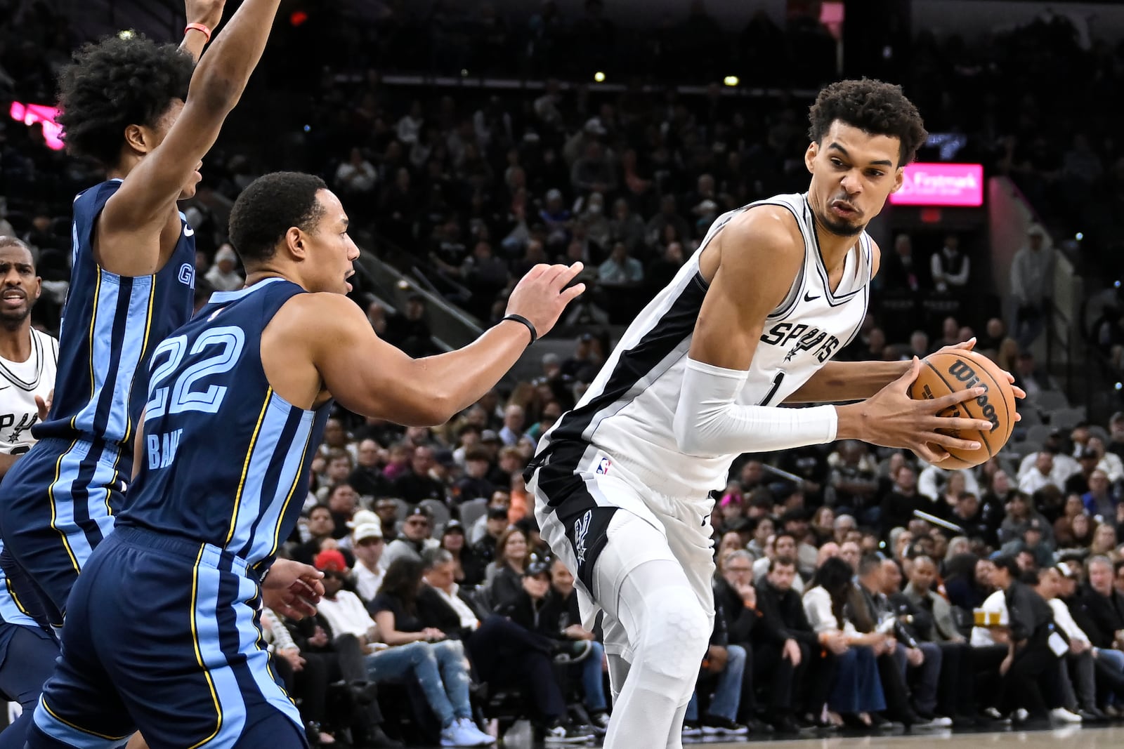 San Antonio Spurs' Victor Wembanyama (1) drives against Memphis Grizzlies' Desmond Bane (22) and Jaylen Wells during the first half of an NBA basketball game, Friday, Jan. 17, 2025, in San Antonio. (AP Photo/Darren Abate)