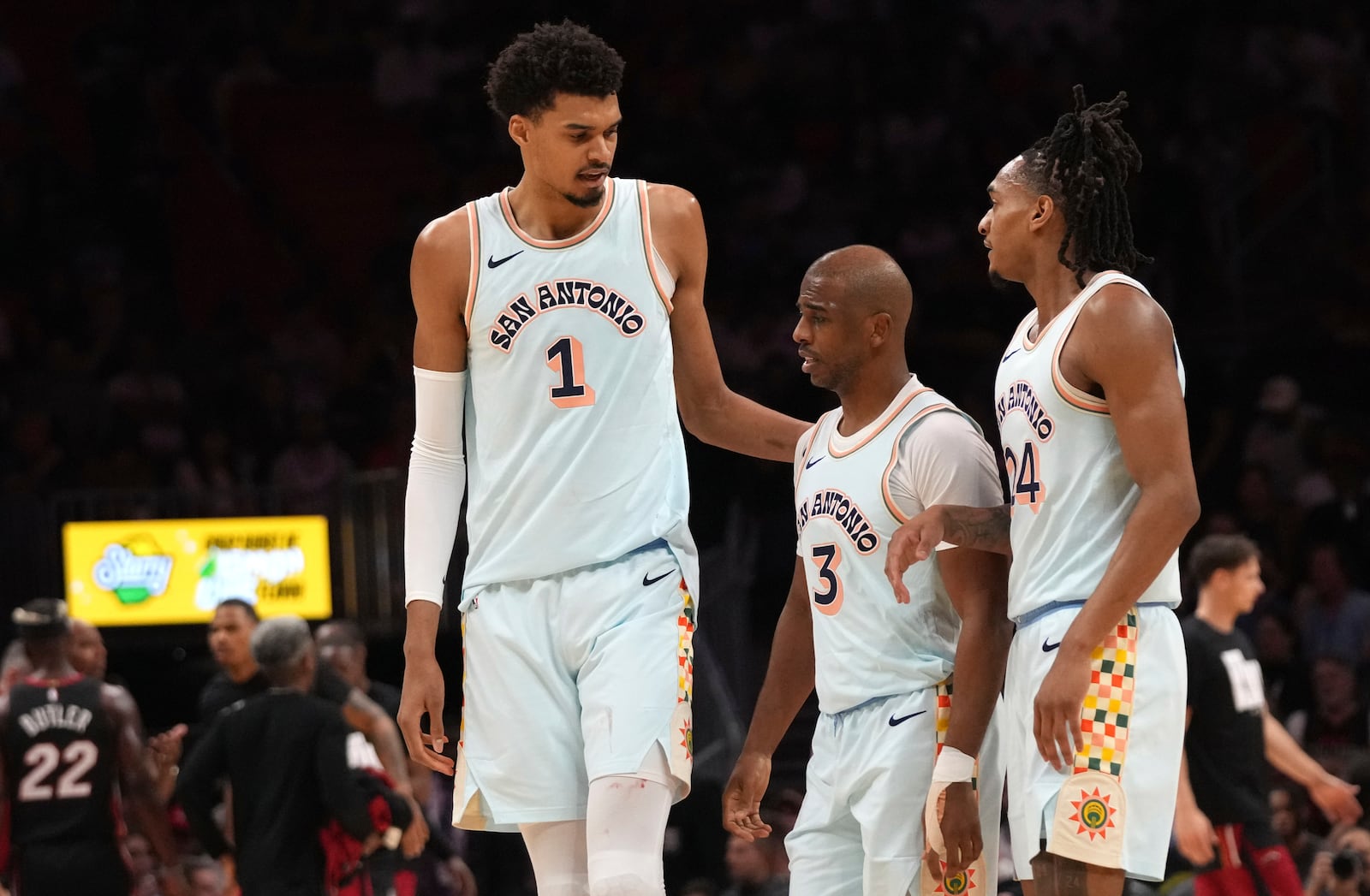 San Antonio Spurs center Victor Wembanyama (1) talks with guard Chris Paul (3) and guard Devin Vassell (24) during the first half of an NBA basketball game against the Miami Heat, Sunday, Jan. 19, 2025, in Miami. (AP Photo/Lynne Sladky)