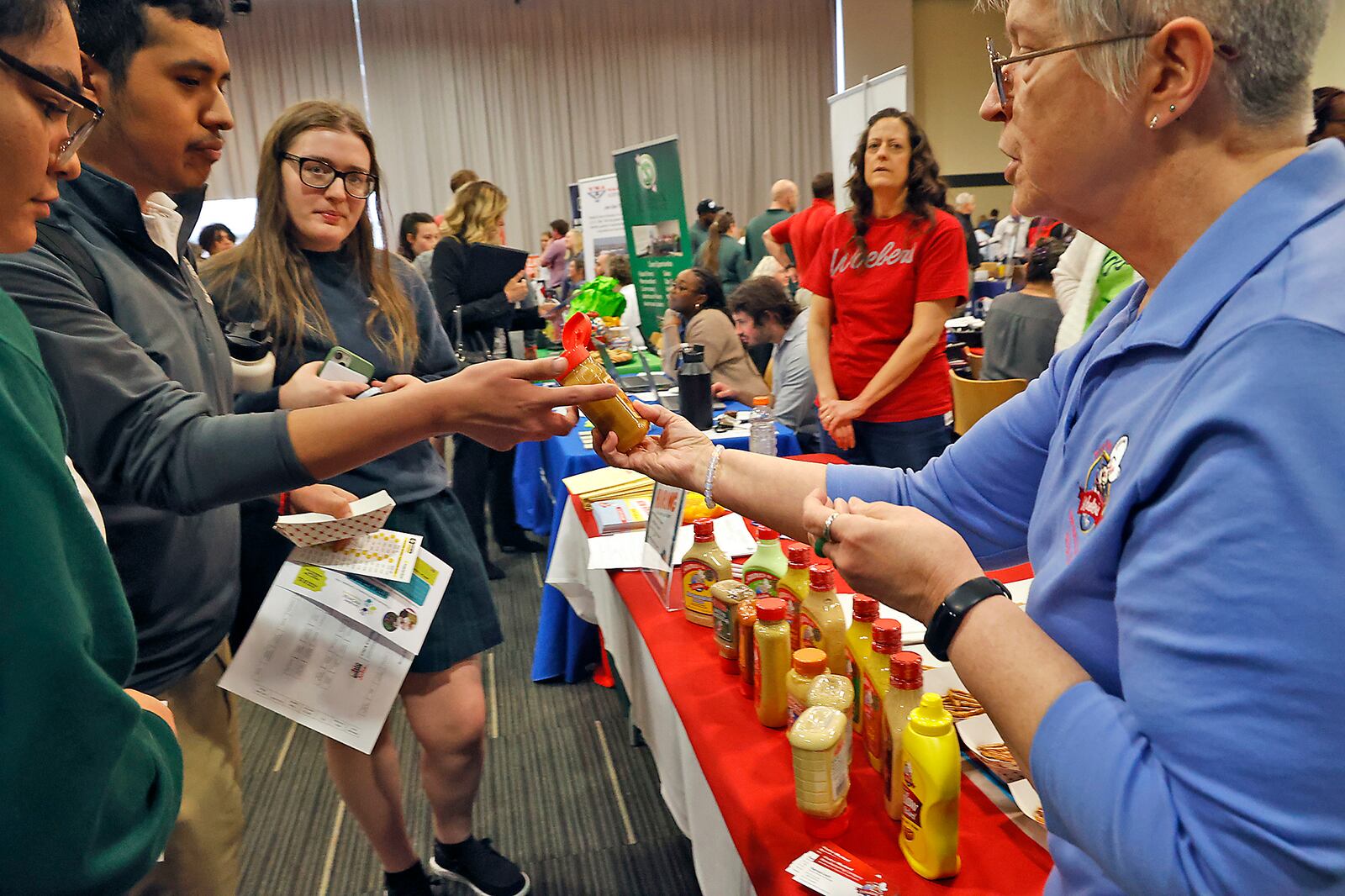 Myra Starr, from Woeber Mustard encourages potential job applicants to sample the Woeber products Wednesday, March 29, 2023 at the 13th Annual Clark County Job Fair at the Hollenbeck-Bayley Conference Center. The event gave job seekers and students from area high schools the chance to meet with over 60 employers from the area and find out what sort of jobs opportunities are available. BILL LACKEY/STAFF