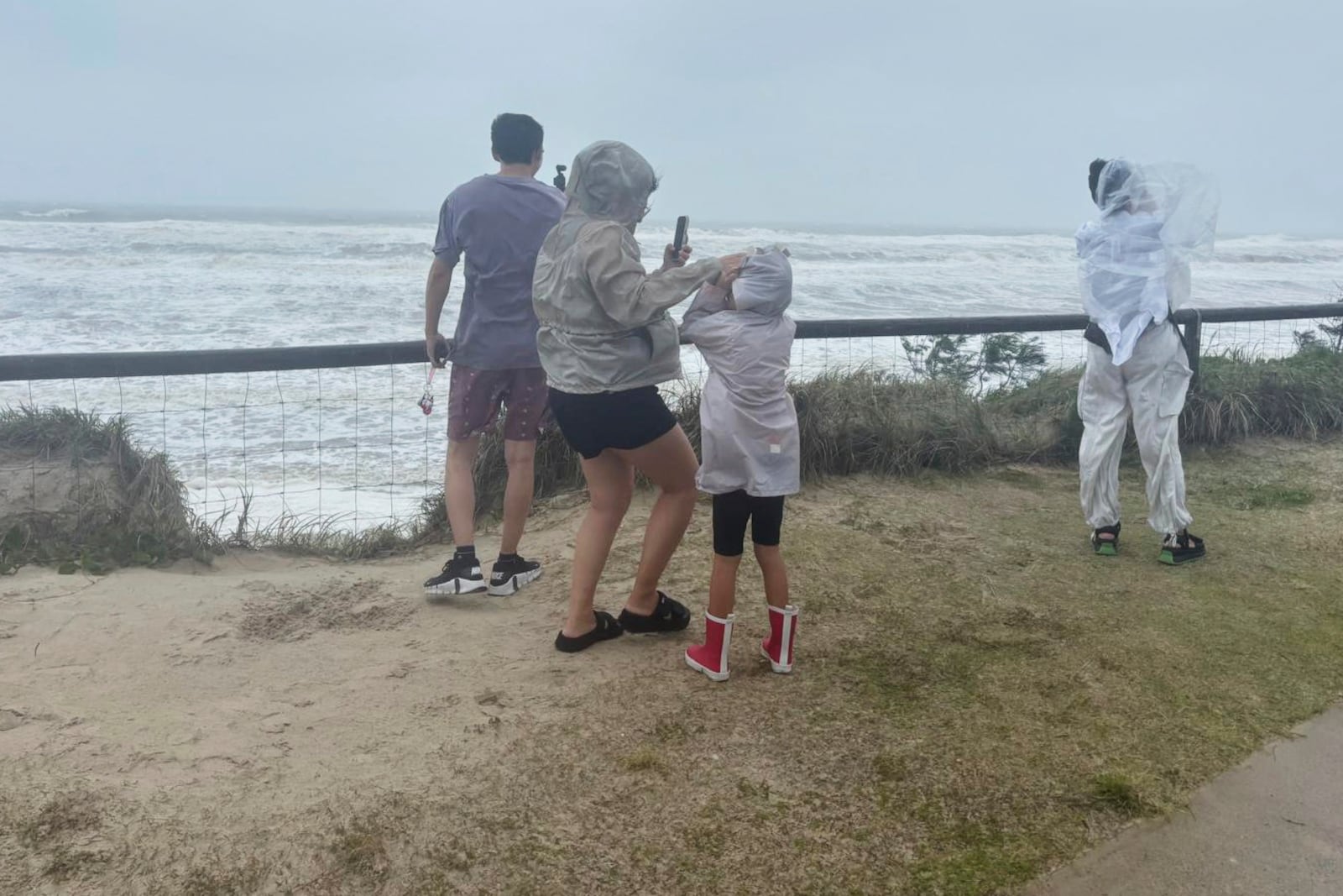 People stand at the beach in high winds as cyclone Alfred arrives on the Gold Coast, Australia, Saturday, March 8, 2025. (AP Photo/John Pye)