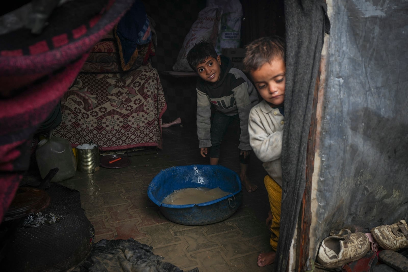 Brothers Belal, 5, and Mohammed Hamad, 7, collect water from their flooded family tent after overnight rainfall at the refugee tent camp for displaced Palestinians in Deir al-Balah, central Gaza Strip, Tuesday, Dec. 31, 2024. (AP Photo/Abdel Kareem Hana)