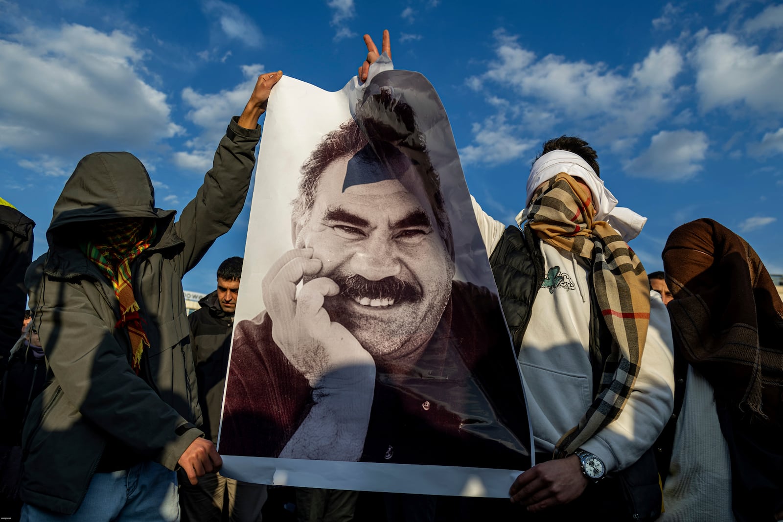 Youngsters hold a photograph of the jailed leader of the rebel Kurdistan Workers' Party, or PKK, Abdullah Ocalan as they gather to watch live on a tv screen a Pro-Kurdish Peoples' Equality and Democracy Party, or DEM, delegation members releasing an statement from Ocalan, in Diyarbakir, Turkey, Thursday, Feb. 27, 2025. (AP Photo/Metin Yoksu)