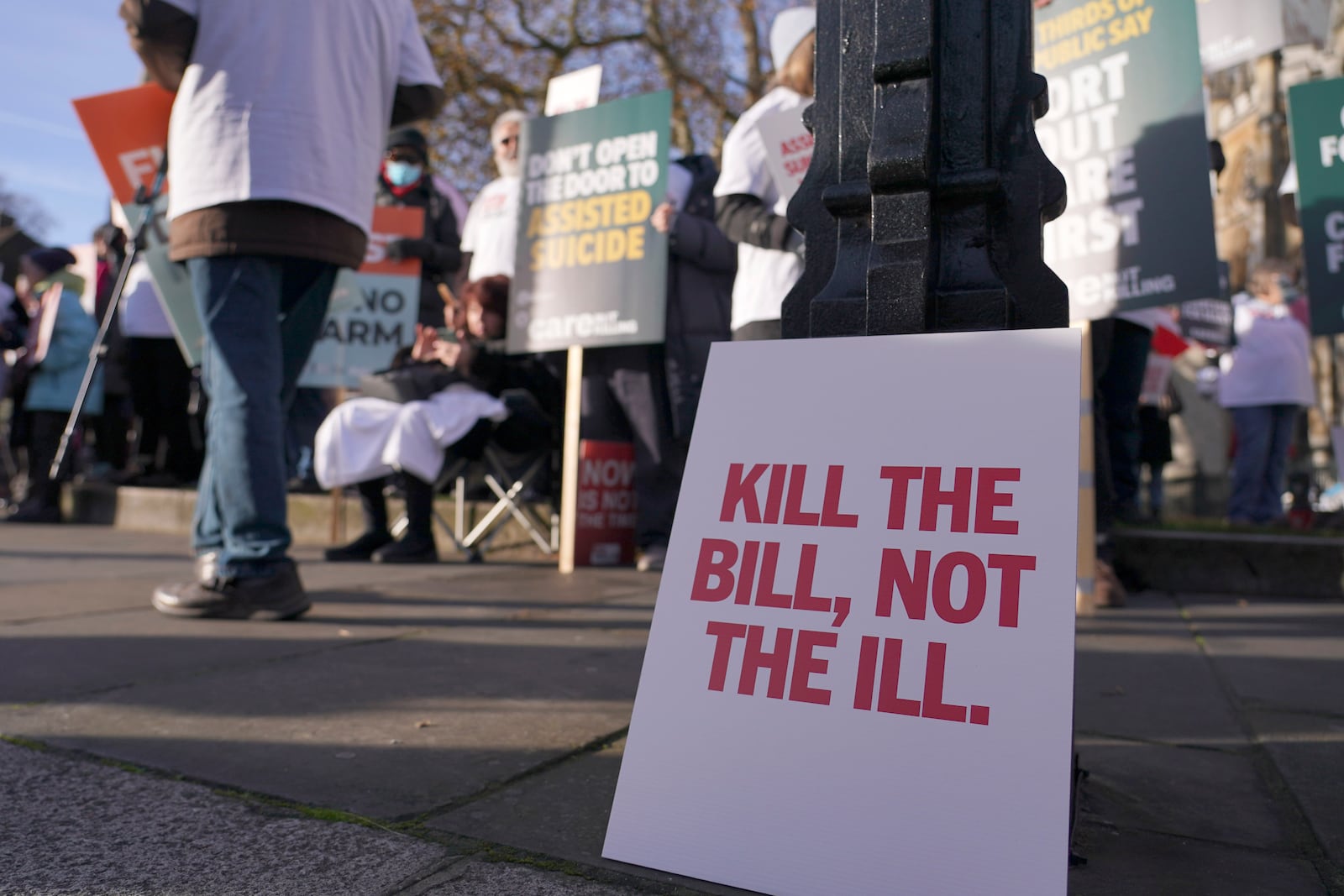 A poster leans on a lambpost as protesters demonstrate in front of Parliament in London, Friday, Nov. 29, 2024 as British lawmakers started a historic debate on a proposed to help terminally ill adults end their lives in England and Wales.(AP Photo/Alberto Pezzali)