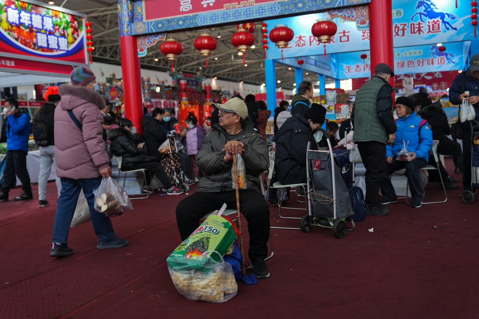 Elderly people with their purchased goods rest as people shop at a New Year bazaar set up for the upcoming Chinese Lunar New Year, in Beijing on Jan. 13, 2025. (AP Photo/Andy Wong)