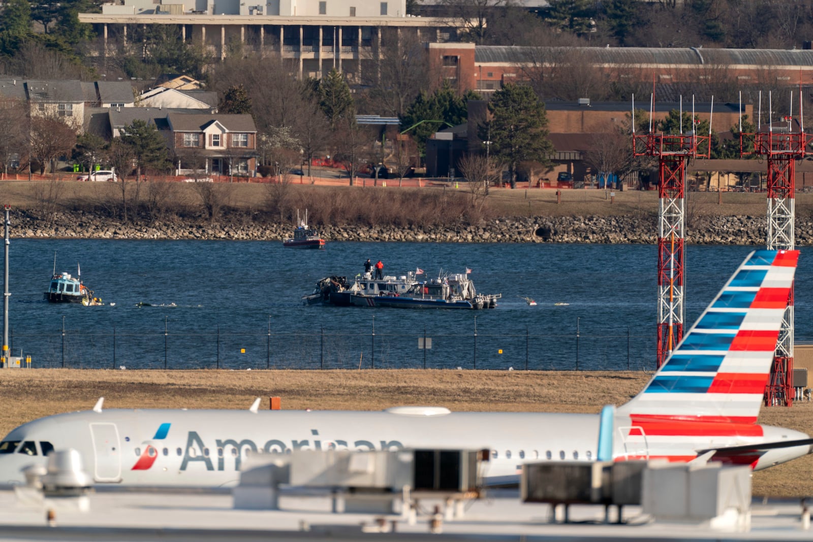 Police and coast guard boats are seen around a wreckage site in the Potomac River as an American Airlines plane passes in the foreground at Ronald Reagan Washington National Airport, Saturday, Feb. 1, 2025, in Arlington, Va., (AP Photo/Jose Luis Magana)