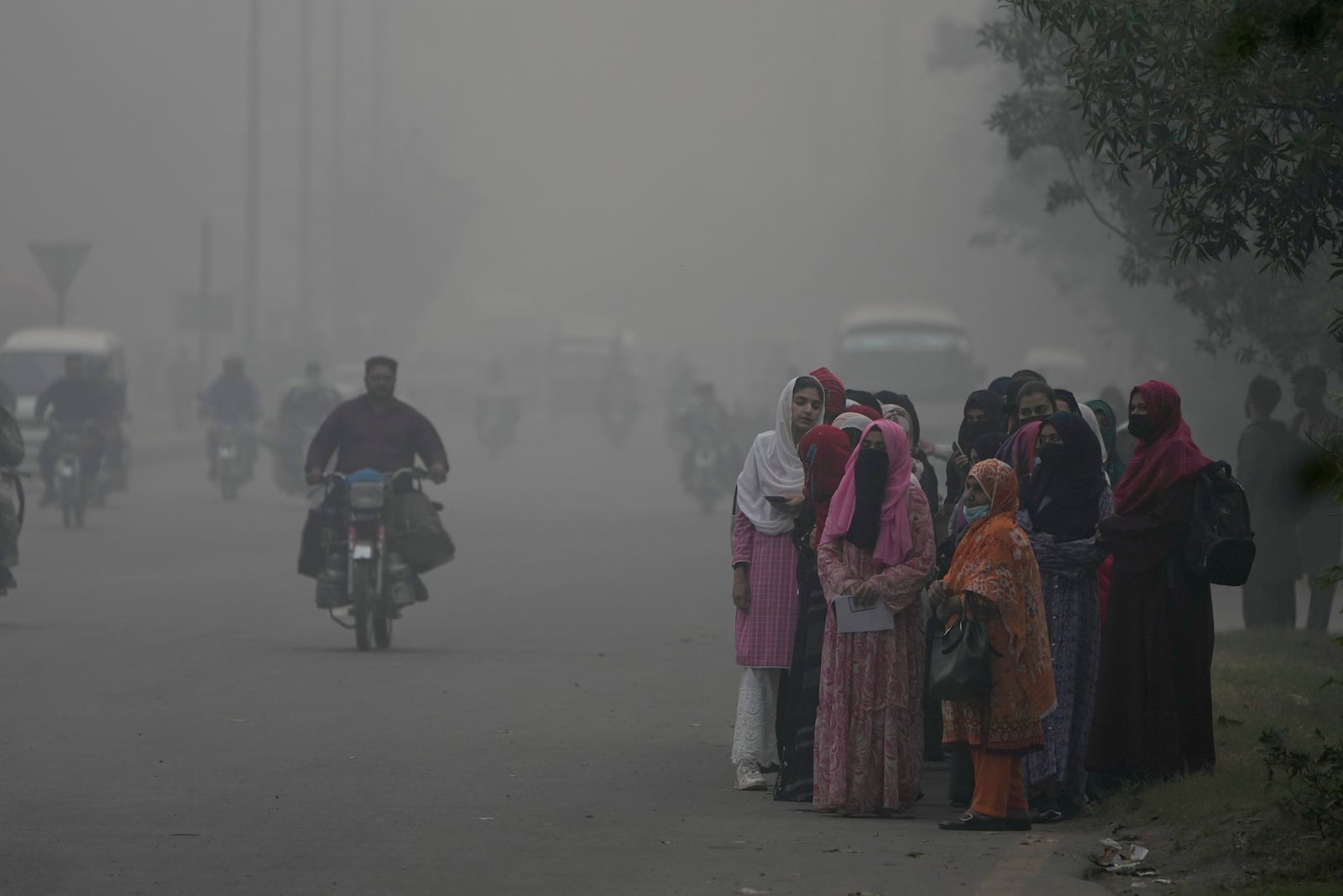 Students wait for transport at a roadside as smog envelops the area of Lahore, Pakistan, Friday, Nov. 8, 2024. (AP Photo/K.M. Chaudary)