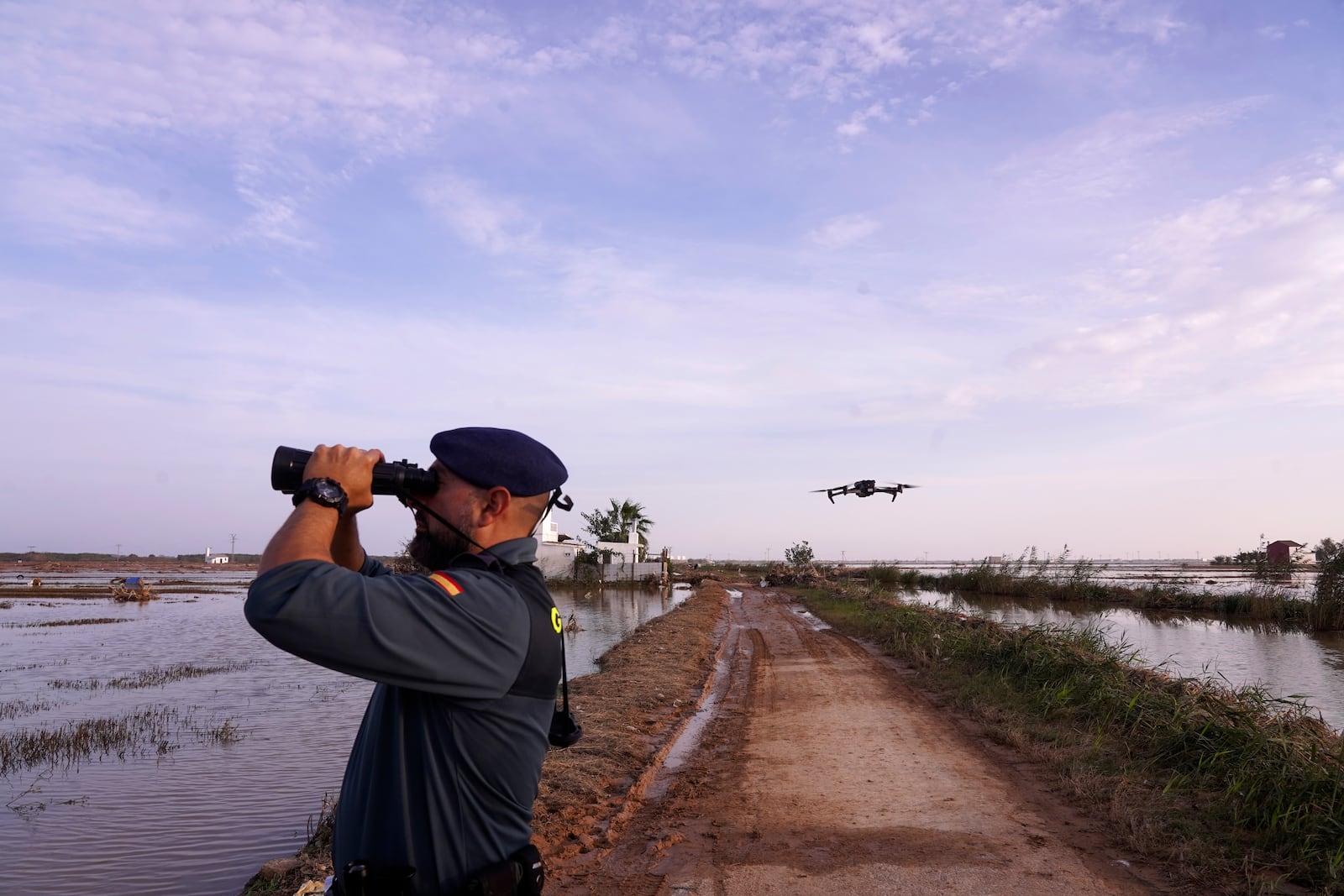 As the search for bodies continues, a Civil Guard looks though binoculars as a drone flies nearby at the mouth of the Poyo ravine in the La Albufera natural lake near Puerto de Catarroja, Valencia on the outskirts of Valencia, Spain, Tuesday, Nov. 5, 2024. (AP Photo/Alberto Saiz)