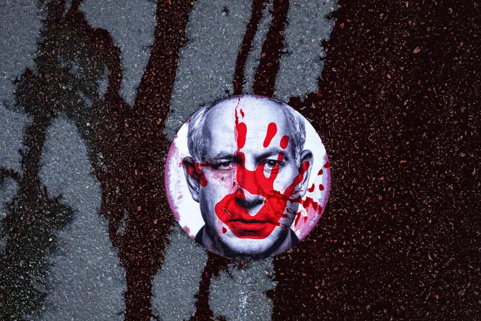 FILE - Supporters of Israelis held hostage by Hamas in Gaza stuck a sticker with the face of Israeli Prime Minister Benjamin Netanyahu on a road and poured red liquid, symbolizing blood, over it, in Jerusalem, Feb. 17, 2025. (AP Photo/Ohad Zwigenberg, File)