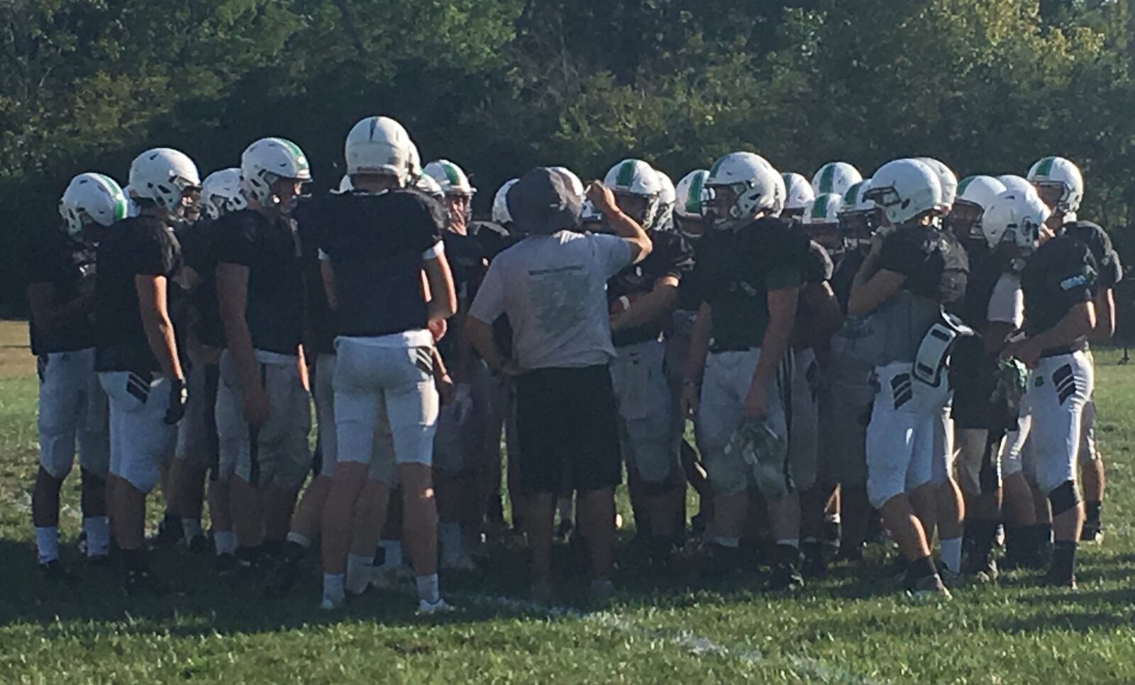 Badin coach Nick Yordy (middle, wearing hat) talks to his team at the end of Wednesday’s practice in Hamilton. The Rams will open the season against Ross on Friday in the Skyline Chili Crosstown Showdown at Hamilton’s Virgil Schwarm Stadium. RICK CASSANO/STAFF