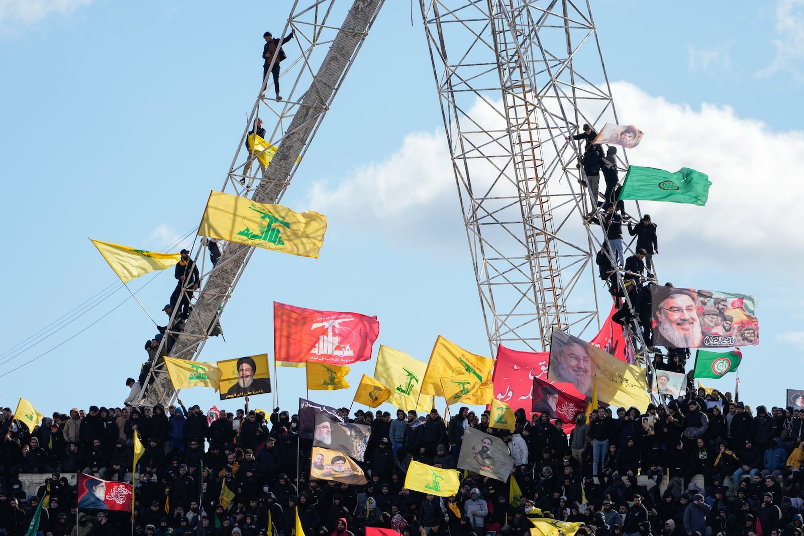 Mourners wave Hezbollah flags, right, as the trailer carrying the coffins containing the bodies of Hezbollah's former leader Hassan Nasrallah and his cousin and successor Hashem Safieddine drives through the crowd at the beginning of a funeral procession in the Sports City Stadium in Beirut, Lebanon, Sunday, Feb. 23, 2025. (AP Photo/Hussein Malla)