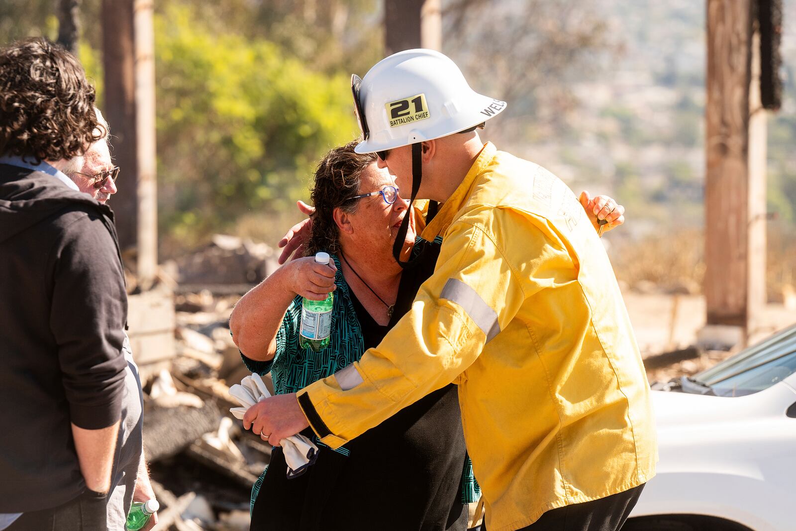 Fawn Parish hugs battalion chief Robert Welsbie, Friday, Nov. 8, 2024, as his firefighters help sift through rubble at her home, which was destroyed by the Mountain Fire in Camarillo, Calif., (AP Photo/Noah Berger)