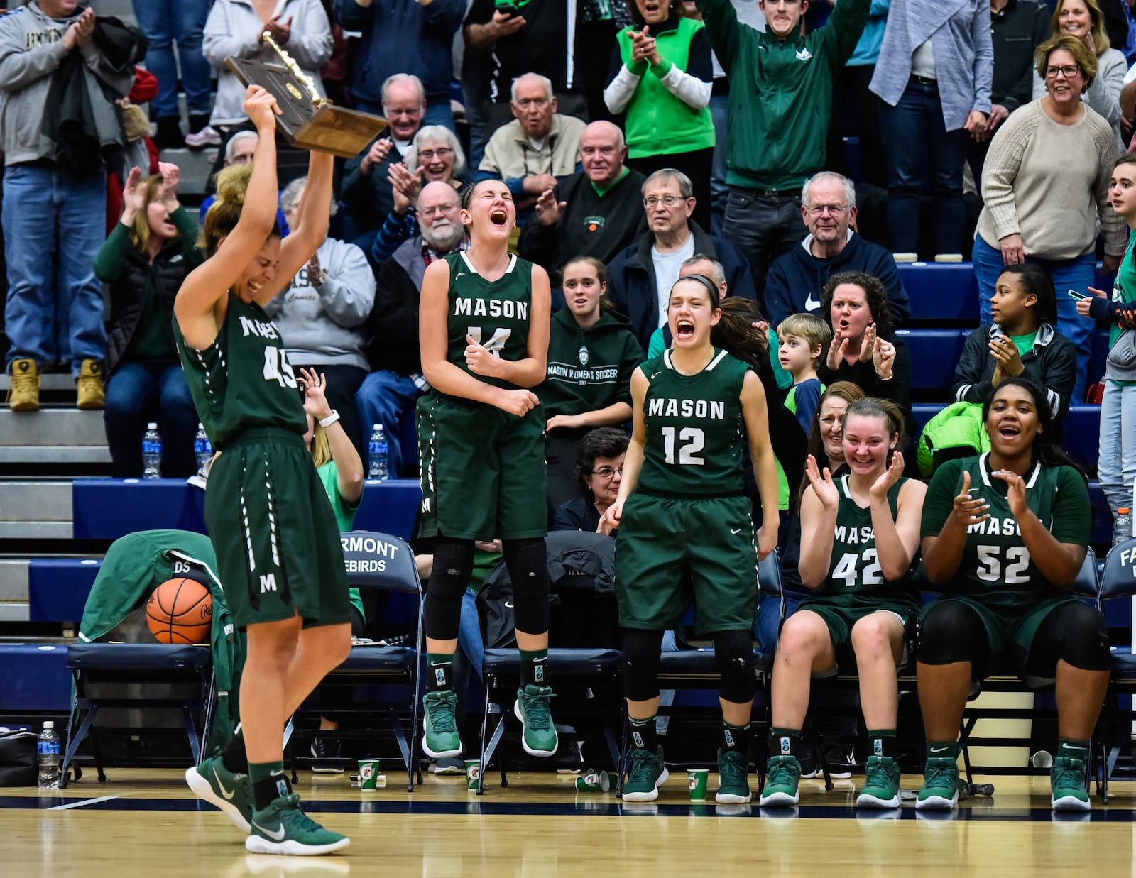 Mason’s Tihanna Fulton (45) hoists the Division I regional championship trophy as teammates Ashley Wells (14), Megan Wagner (12), Anna Brinkmann (42) and Secret Hughes (52) react after Saturday night’s victory over Lakota West at Fairmont’s Trent Arena . NICK GRAHAM/STAFF