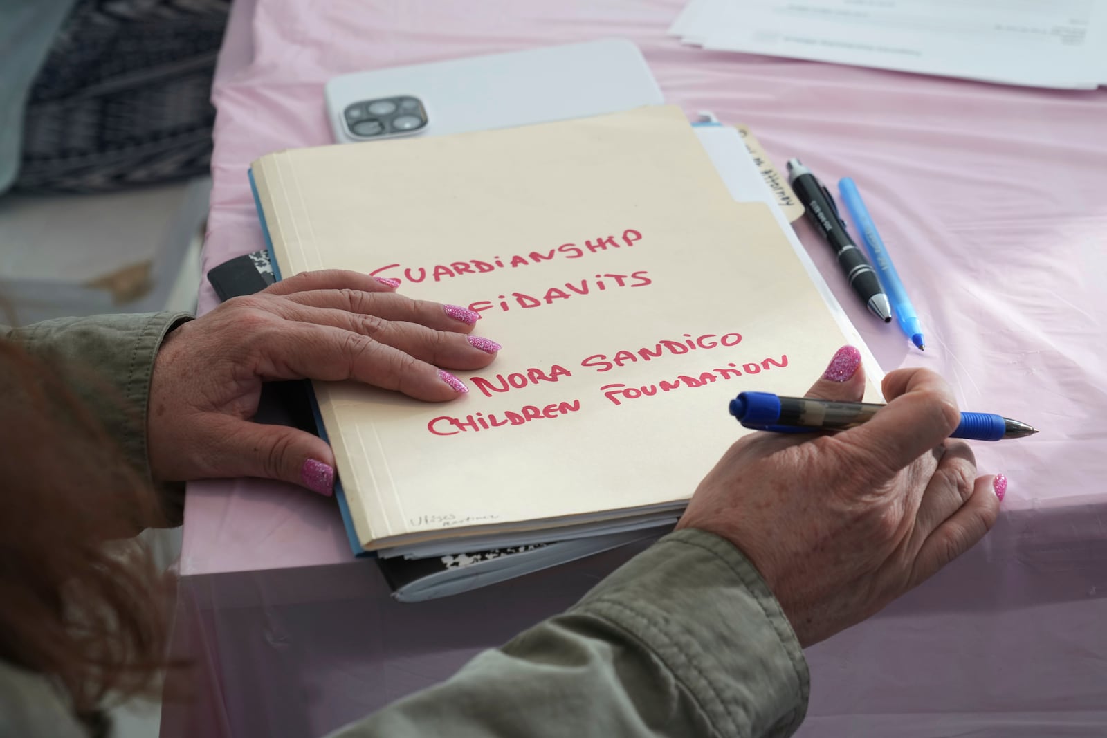 Nora Sandigo holds a folder with documents signed by families giving her legal guardianship of their children, Sunday, Jan. 19, 2025, in Miami. Since December, Sandigo has become the legal guardian of at least 30 children. She has been doing so for 15 years and is the legal guardian to more than 2,000 children. (AP Photo/Marta Lavandier)