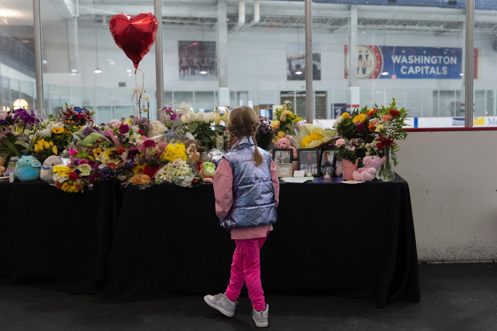 A young girl visits a memorial along the boards at MedStar Capitals Iceplex Sunday, Feb. 2, 2025, in Arlington, Va., for the figure skaters who were among the 67 victims of a mid-air collision between an Army helicopter and an American Airlines flight from Kansas. (AP Photo/Carolyn Kaster)