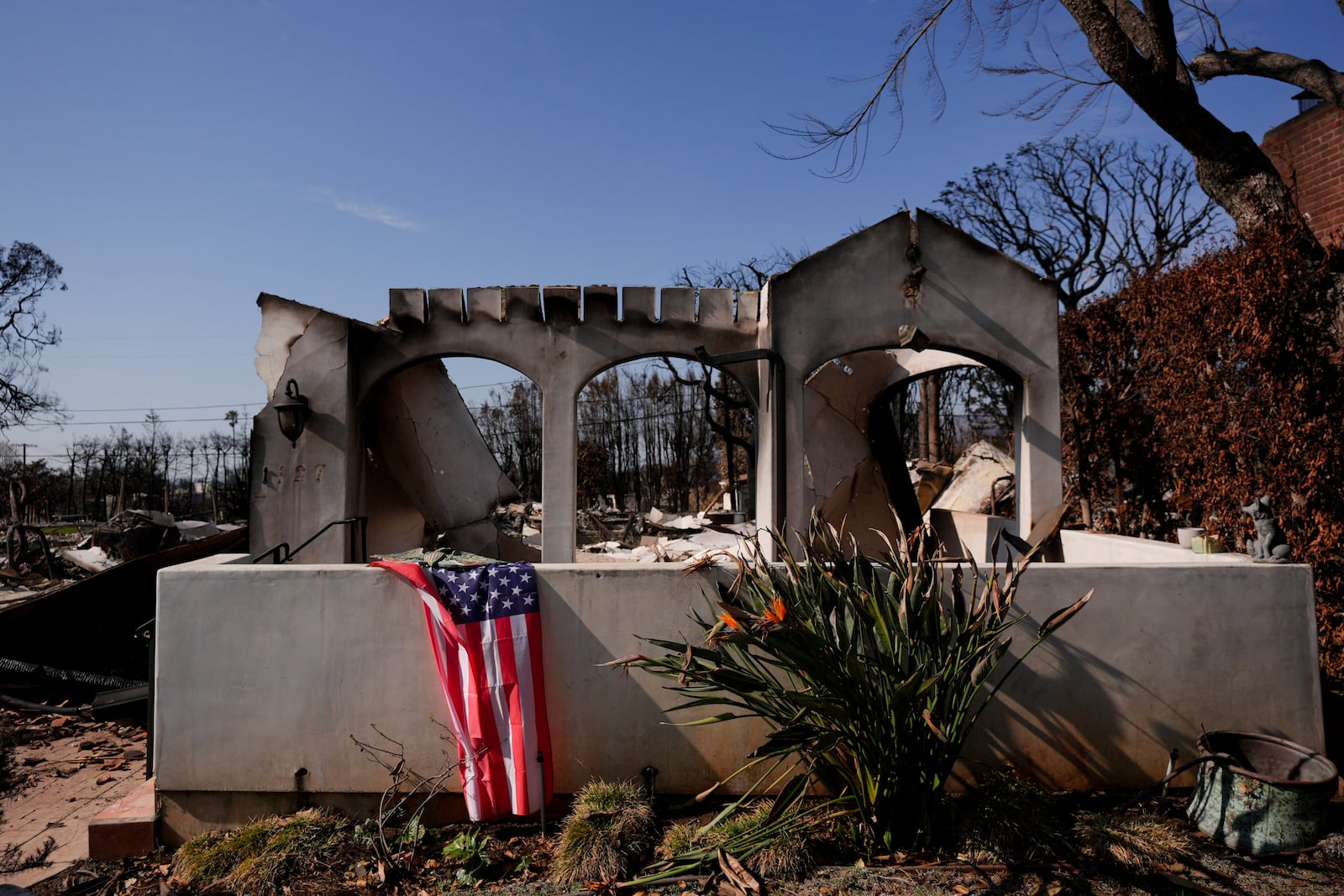 A U.S. flag is draped in front of a fire-ravaged property in the Palisades Fire burn zone in the Pacific Palisades neighborhood of Los Angeles, Tuesday, Jan. 28, 2025. (AP Photo/Jae C. Hong)