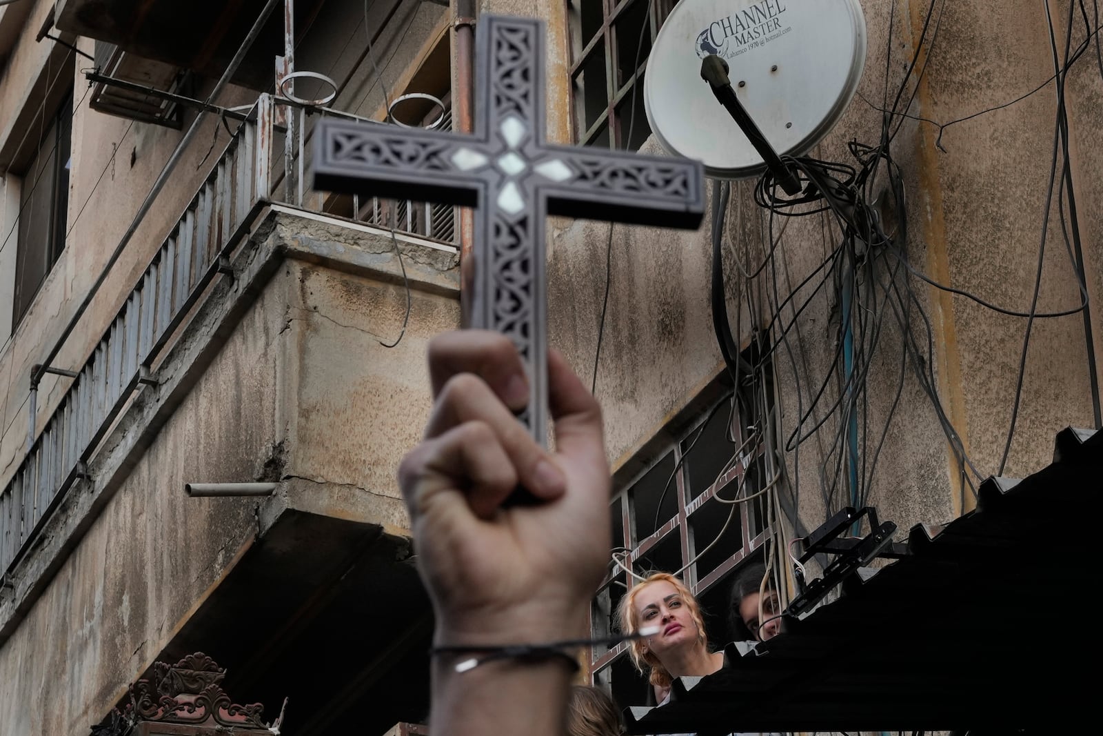 A woman looks at Syrian Christians carrying crosses and shouting slogans in Damascus, Syria, Tuesday, Dec. 24, 2024, during a protest after a Christmas tree was set on fire in Hamah city on Sunday. (AP Photo/Hussein Malla)