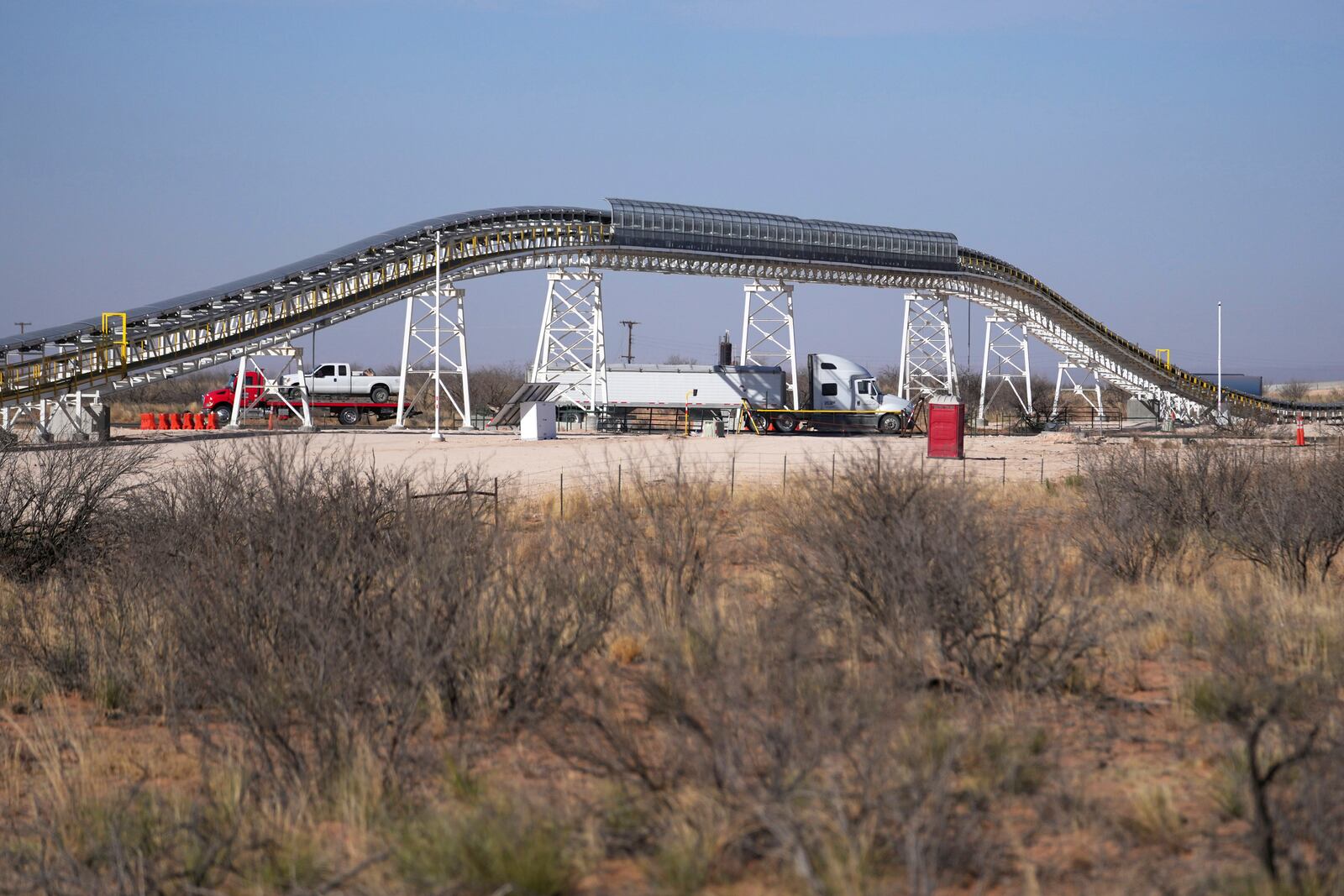 Traffic flows along Route 18 near the Texas/New Mexico state line as a 42-mile conveyor belt by Atlas Energy is seen at a distance carrying sand needed for hydraulic fracturing Wednesday, Feb. 26, 2025, in Kermit, Texas. (AP Photo/Julio Cortez)