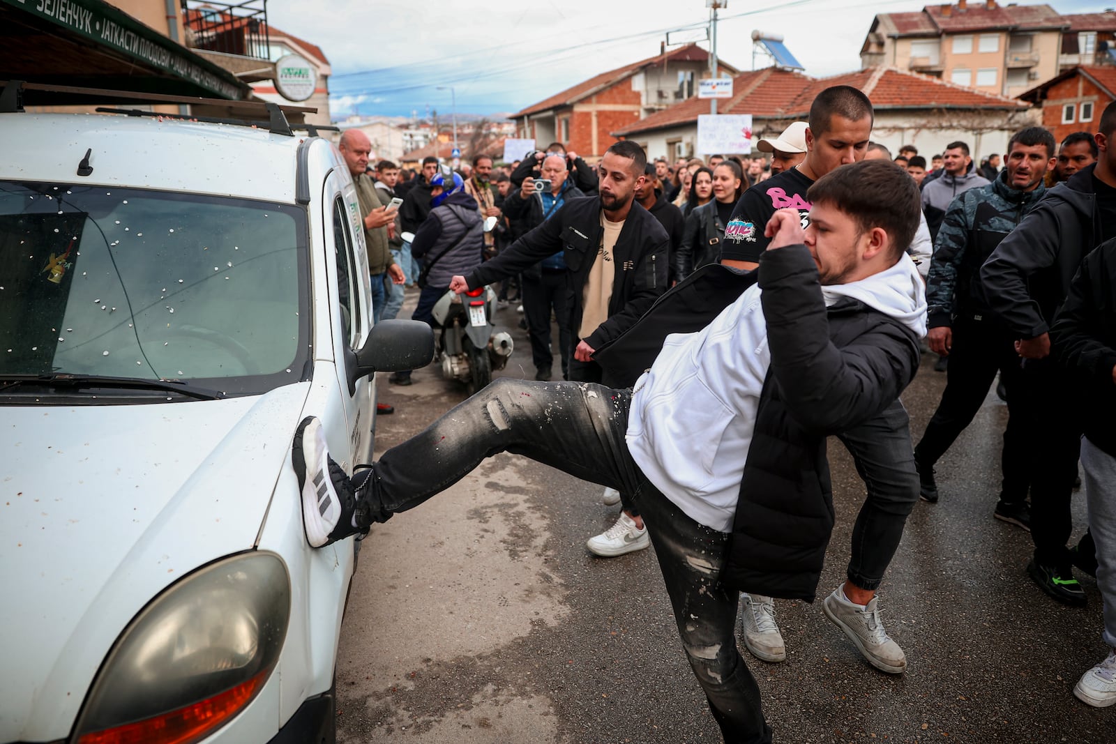 People vandalize a vehicle outside the home of the owner of a nightclub that was the scene of a massive fire, after a vigil for the victims in the town of Kocani, North Macedonia, Monday, March 17, 2025. (AP Photo/Armin Durgut)