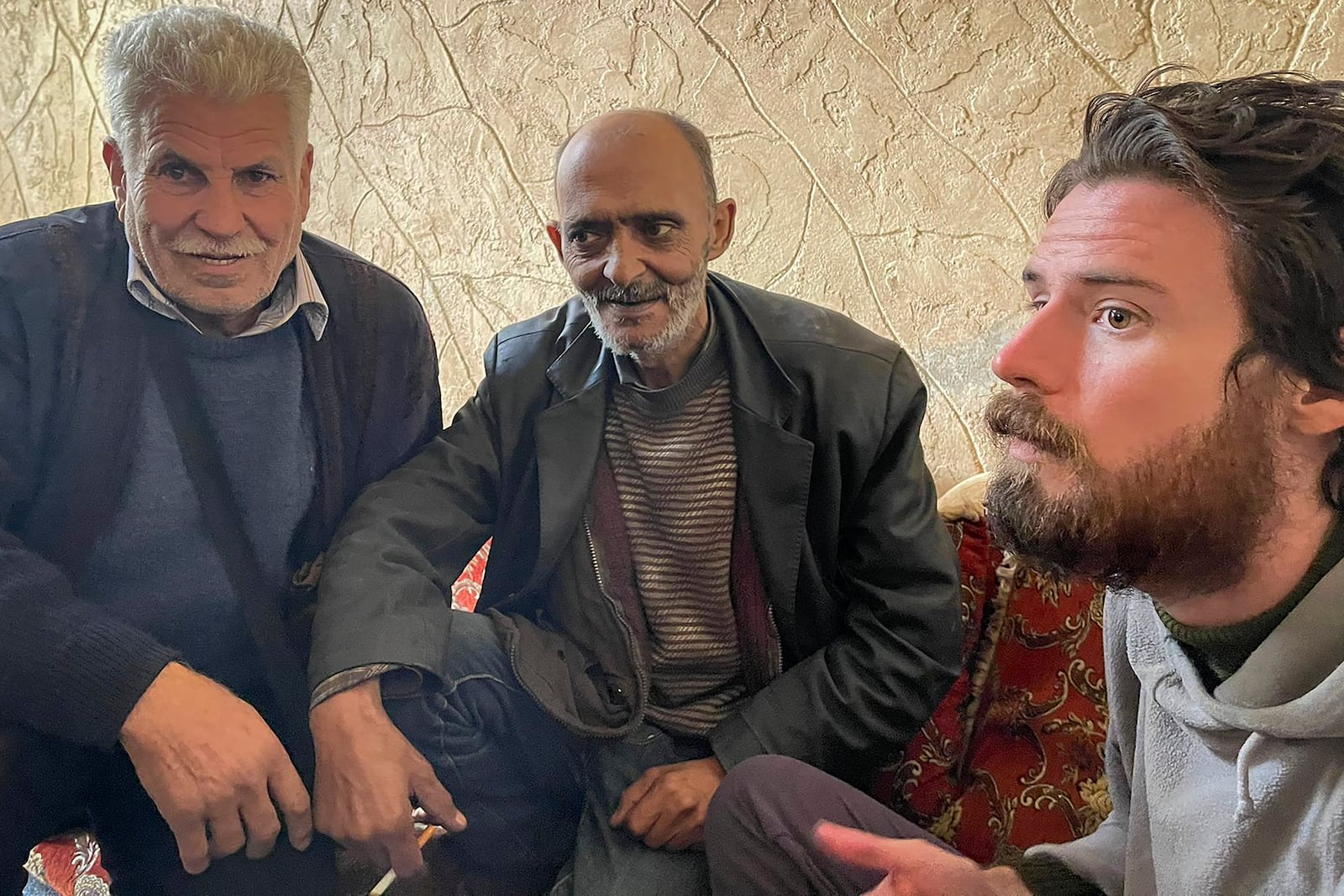 In this photo provided by the Syrian Emergency Task Force, American Travis Timmerman, right, sits with Mosaed al-Rifai, center, who found him in the Syrian desert, and the owner of the house where he took refuge, left, name not available, in Damascus, Syria on Thursday Dec. 12, 2024. (Syrian Emergency Task Force via AP)